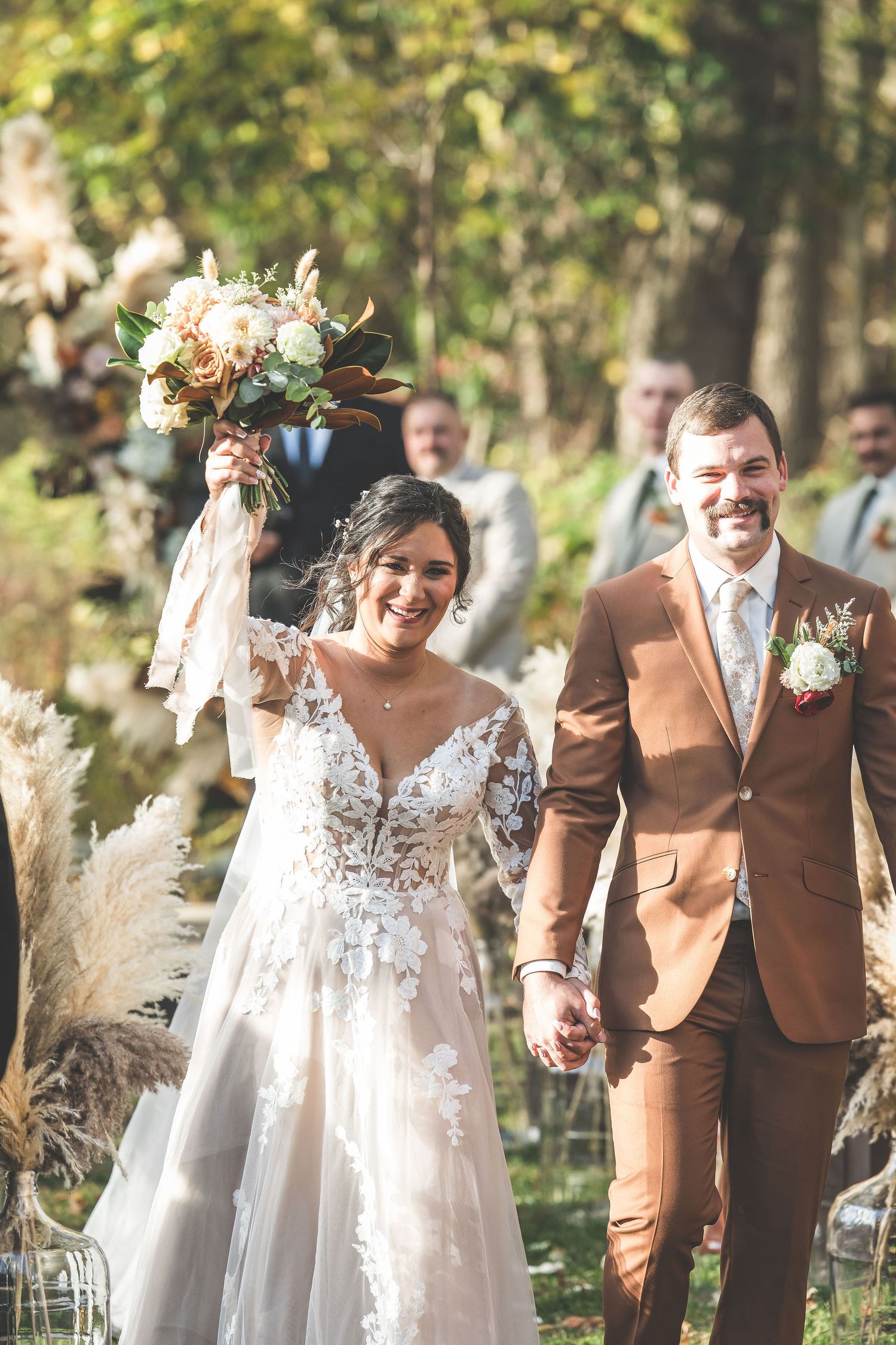 Couple walking down outdoor path with autumn decor and pampas grass arrangements.