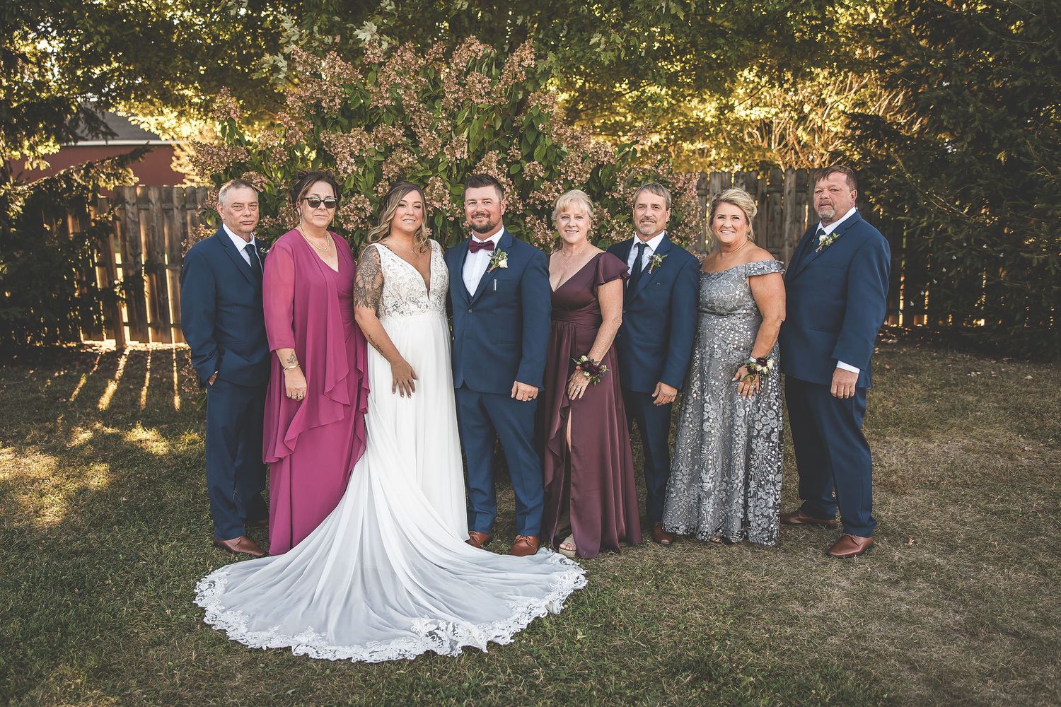 Large wedding party poses for formal group photos in outdoor garden setting.
