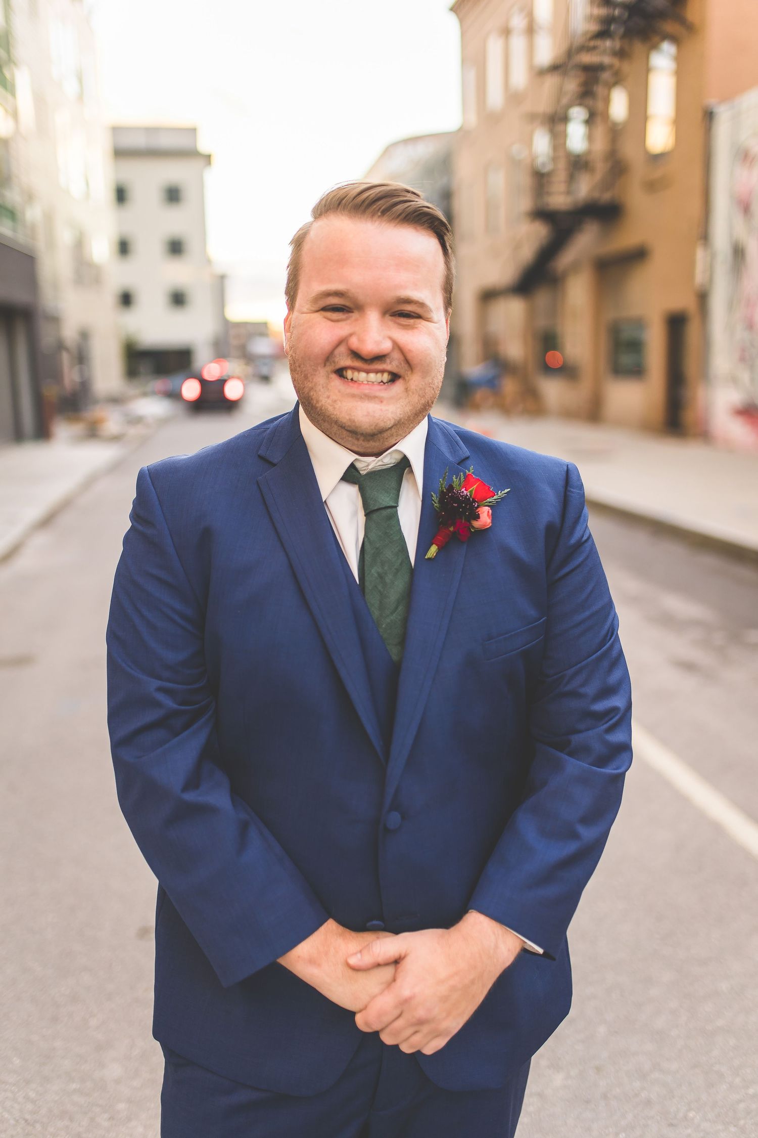 Groom in navy suit with green tie poses on urban street.