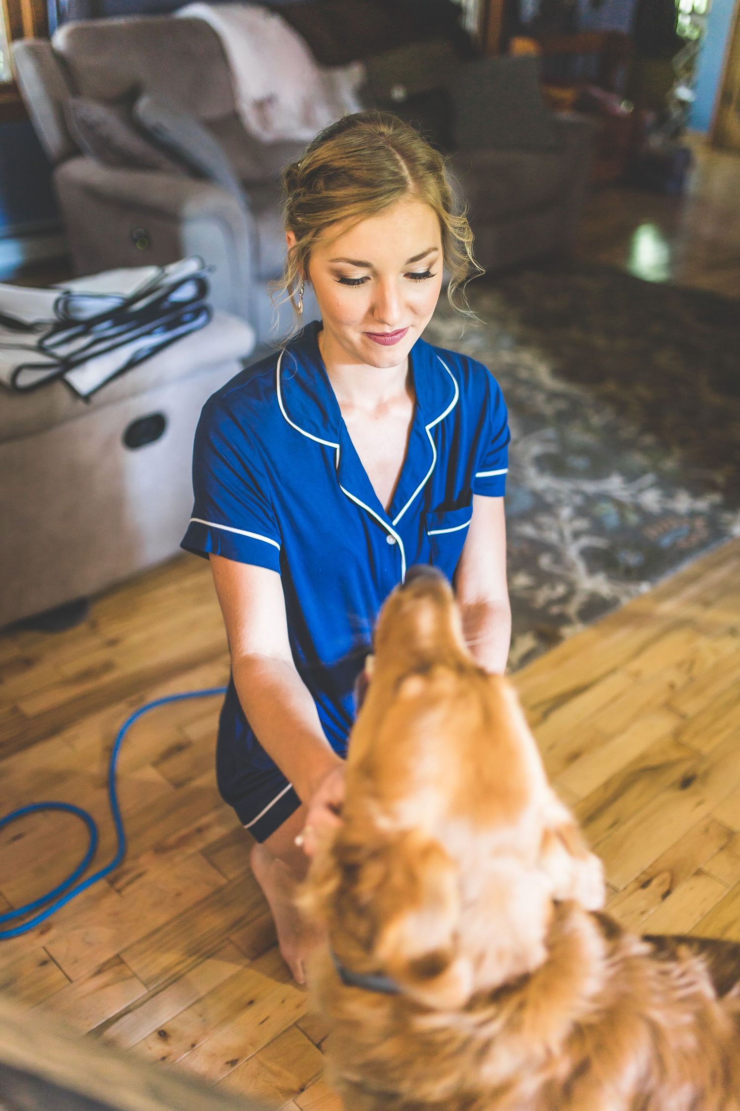 Person in blue robe petting a ginger cat on wooden floor during wedding preparations.