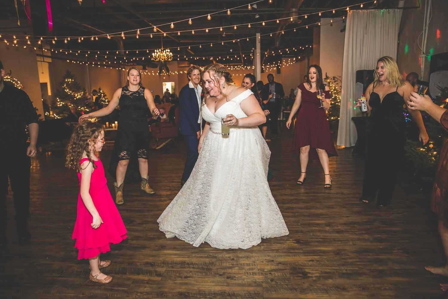Guests dancing at a wedding reception with string lights creating a festive atmosphere.