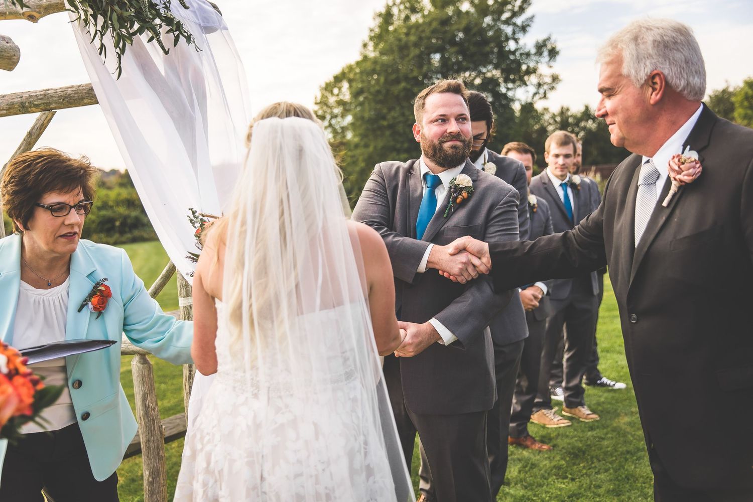 Guests mingle and celebrate at a sunny outdoor wedding reception with white decor.