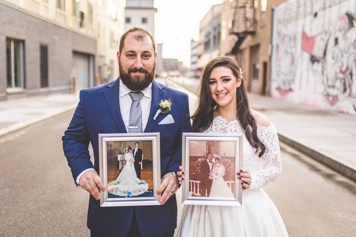 Wedding couple and party members hold up framed photos on city street.