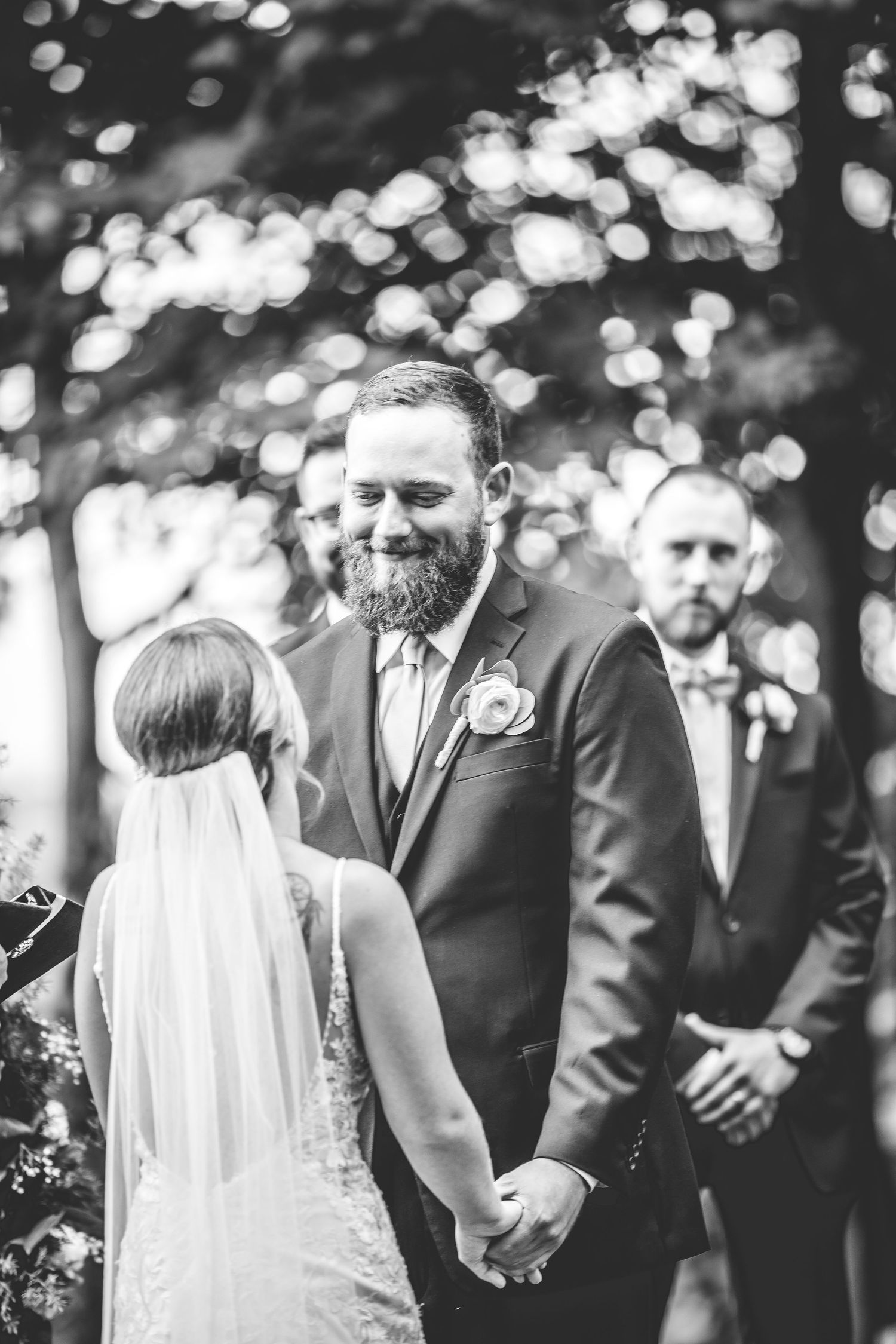 Black and white candid moment during outdoor wedding ceremony with bokeh background.