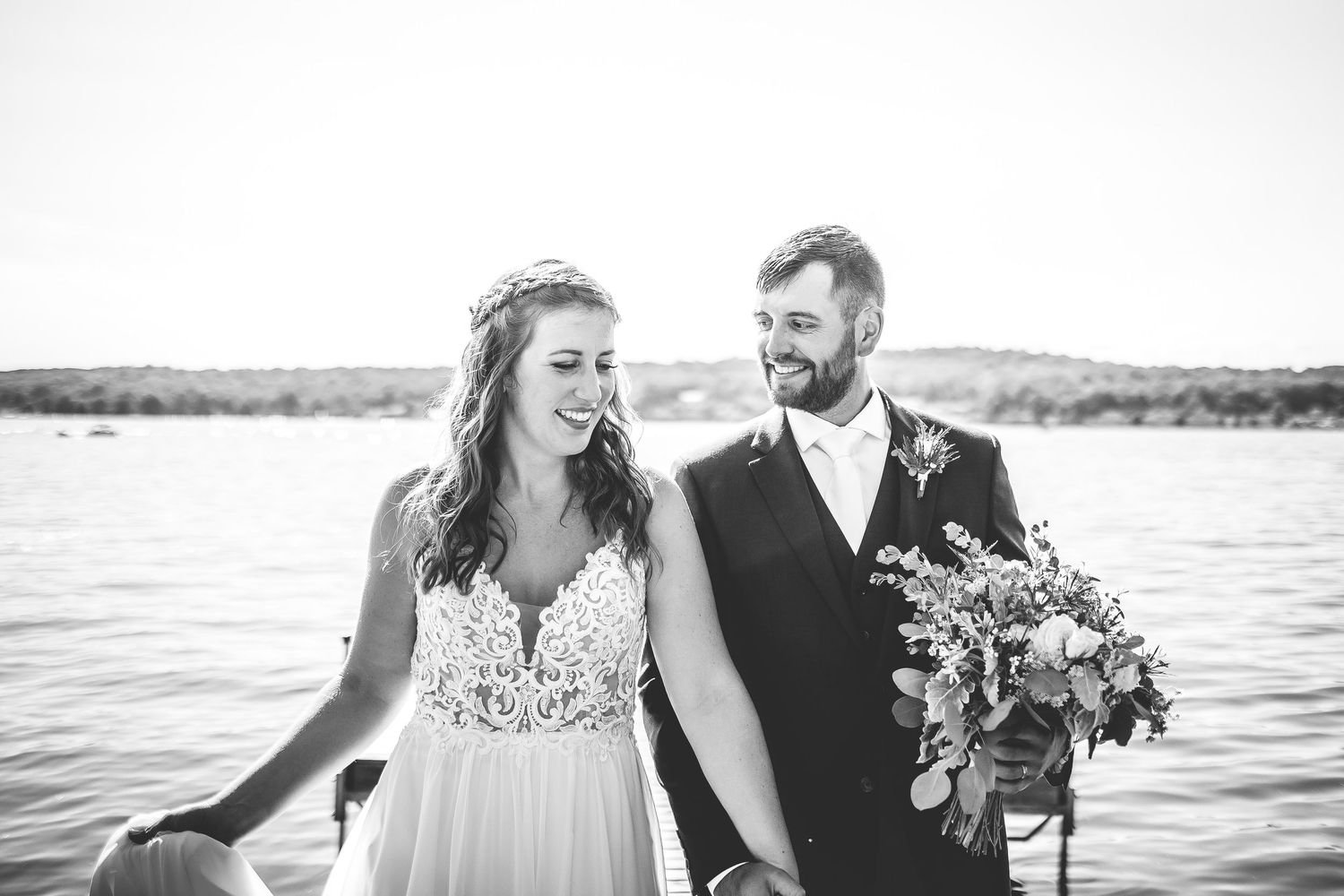 A couple shares a joyful moment by the waterfront in black and white wedding photography.