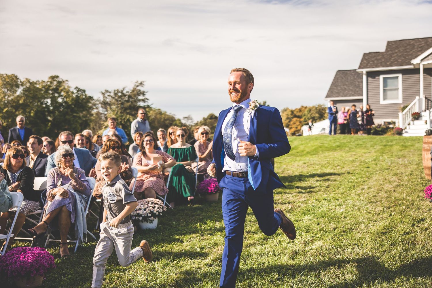 Person in blue suit walks down grassy aisle during outdoor ceremony.