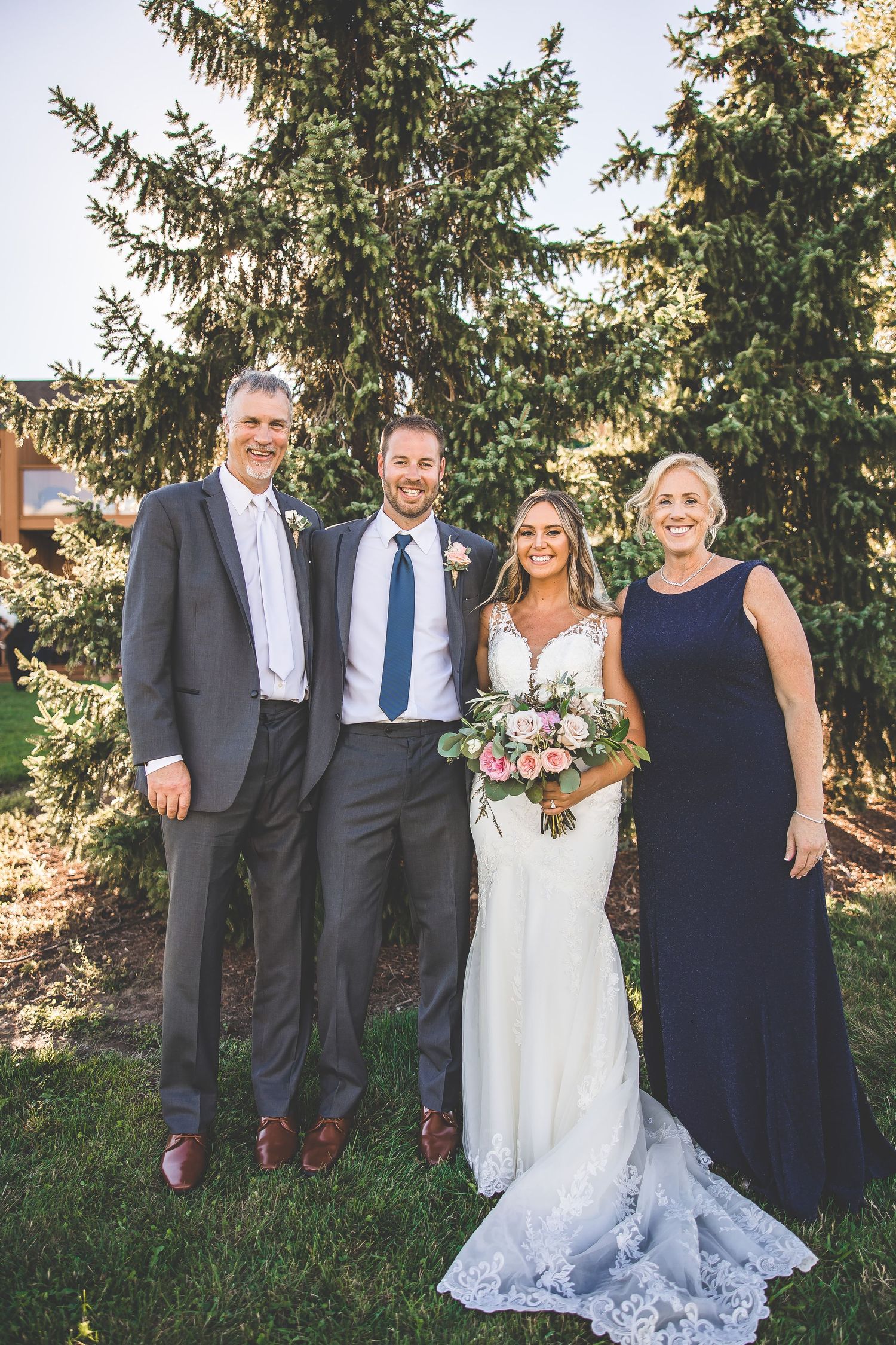 Wedding party portrait with couple and family members posed against natural evergreen backdrop.