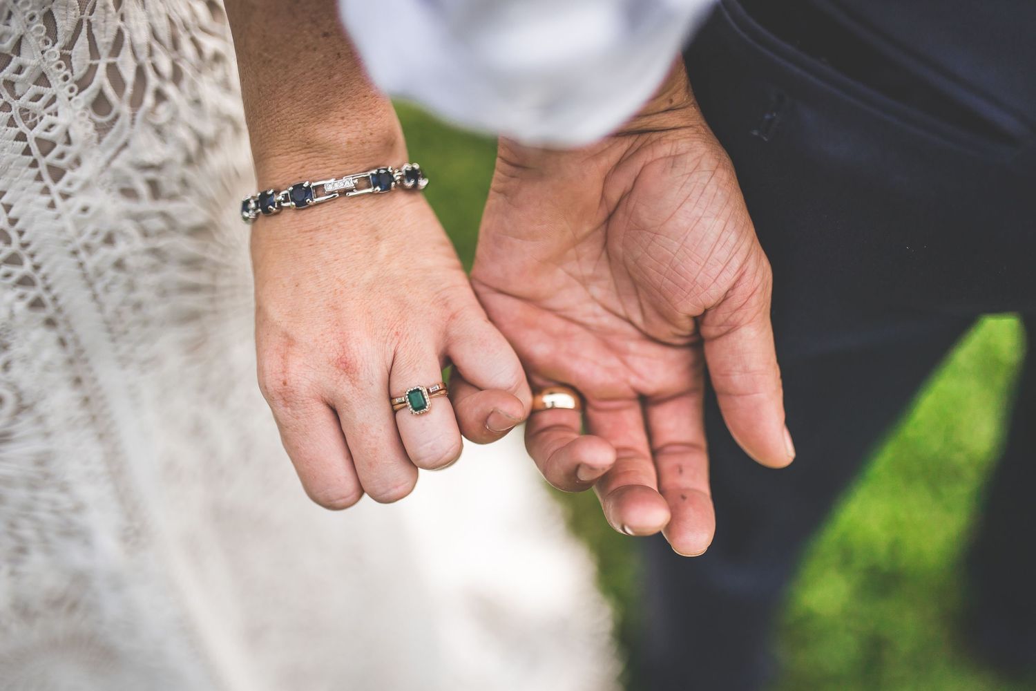 Close-up details of wedding rings and hands against lace dress fabric.