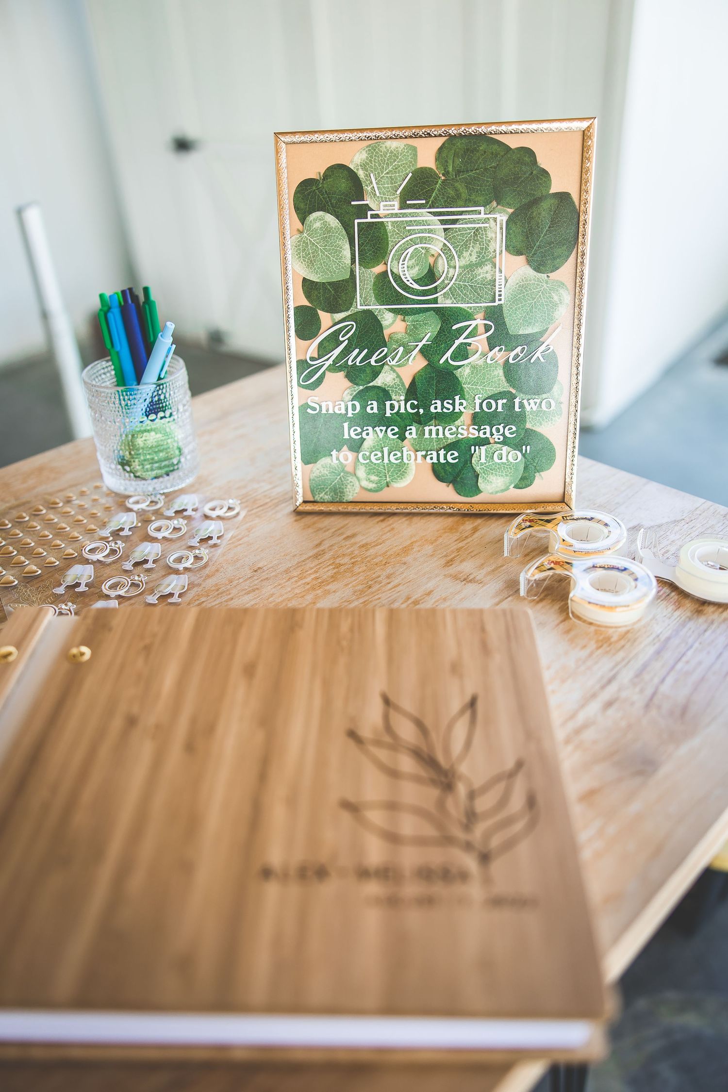 Guest book table setup with greenery decor and signing materials at a wedding reception.
