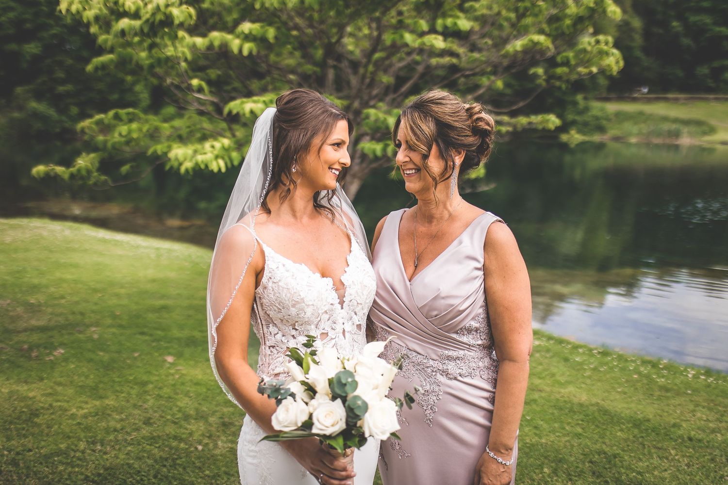 A wedding party poses together outdoors near a serene lake with a fountain feature.