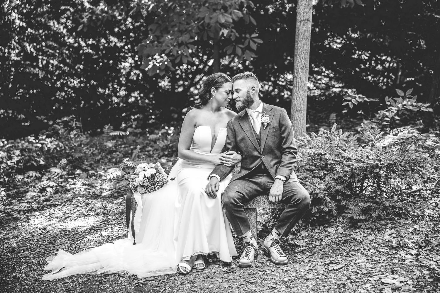 Black and white wedding portrait showcasing the couple relaxing in a natural woodland setting.