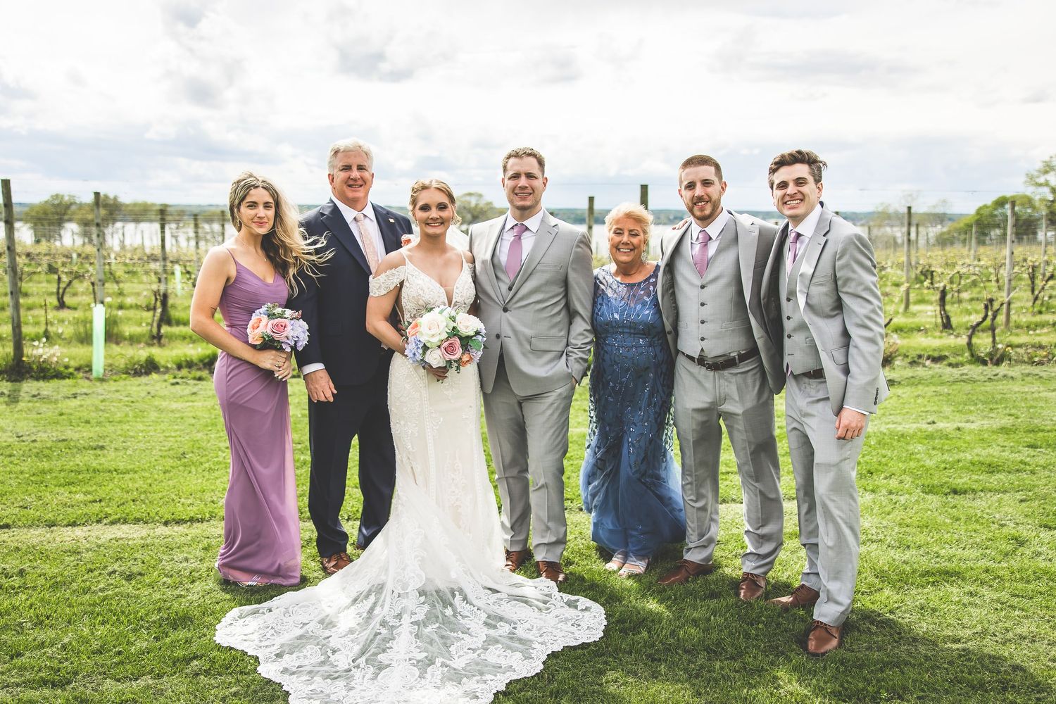 Wedding party members posing and celebrating together in front of vineyard rows.