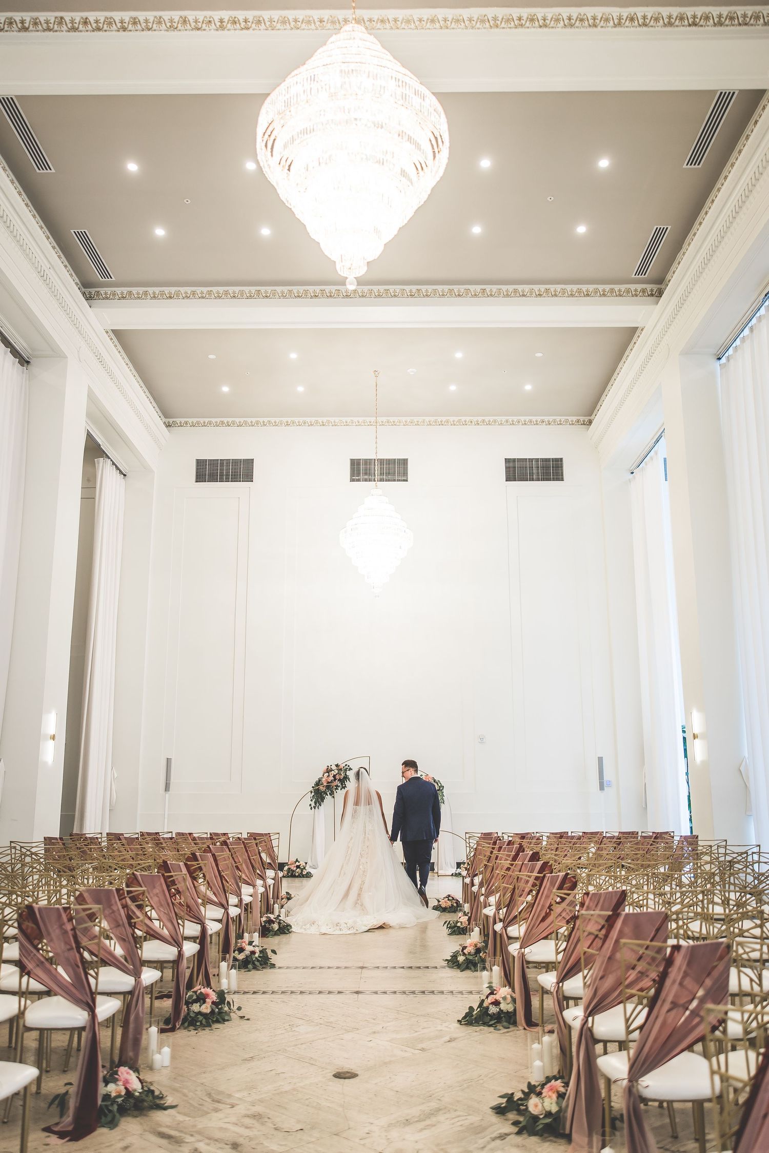 Elegant white wedding venue with crystal chandelier and rows of ceremony chairs.
