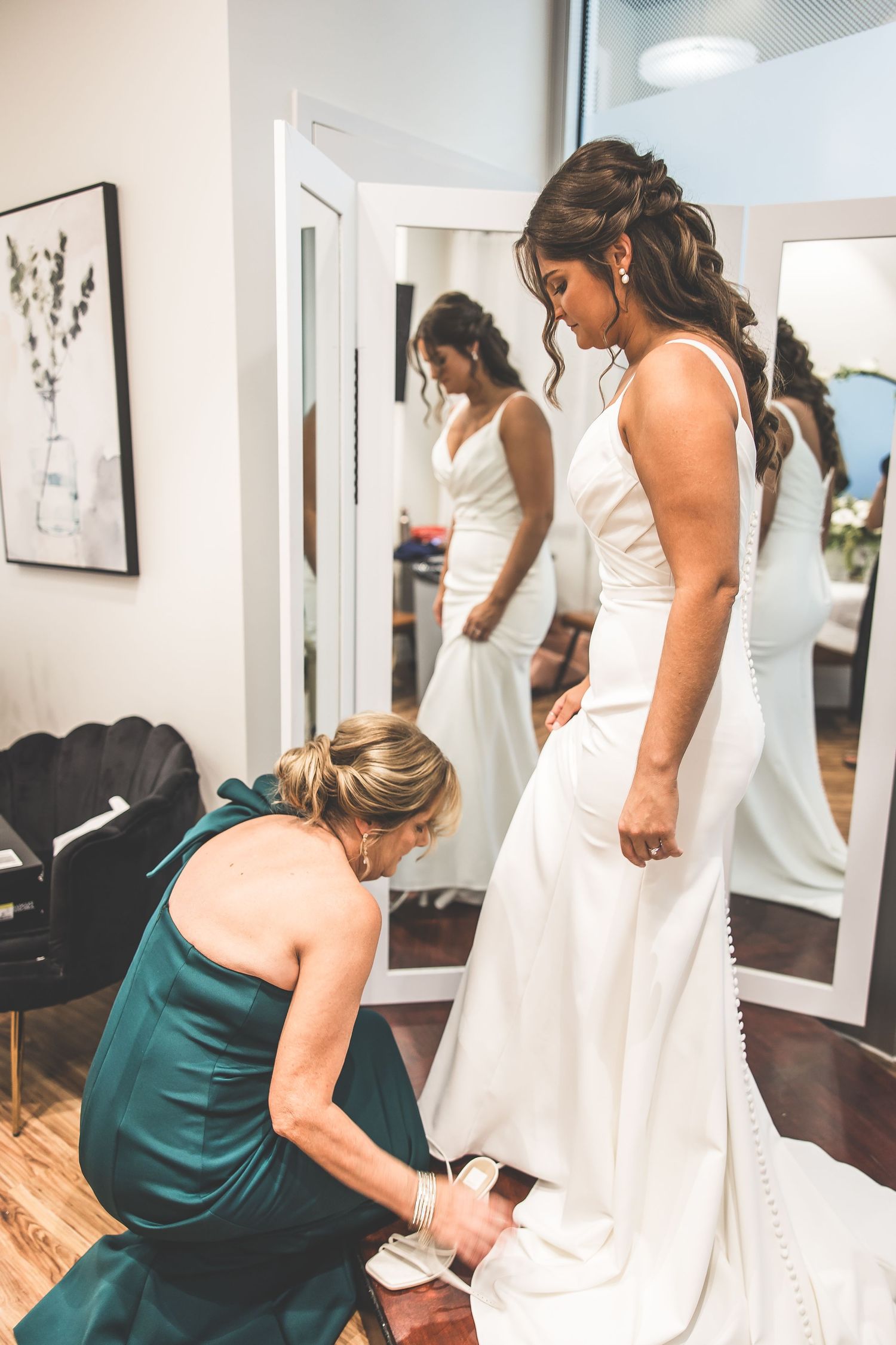 Women in teal dresses assist with wedding dress preparations in a bright indoor setting.