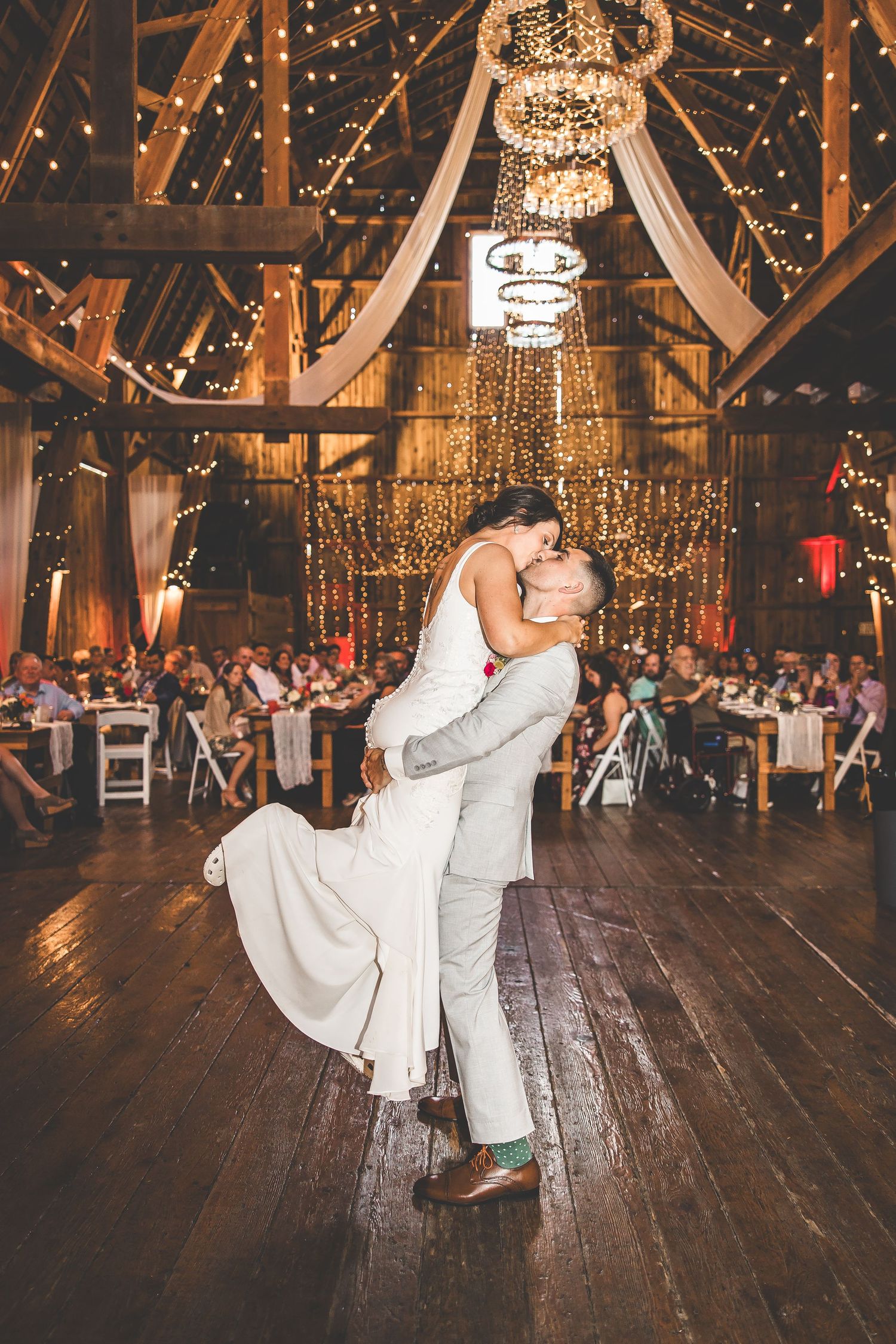 A dramatic dip during the first dance under elegant chandeliers in a rustic barn setting.