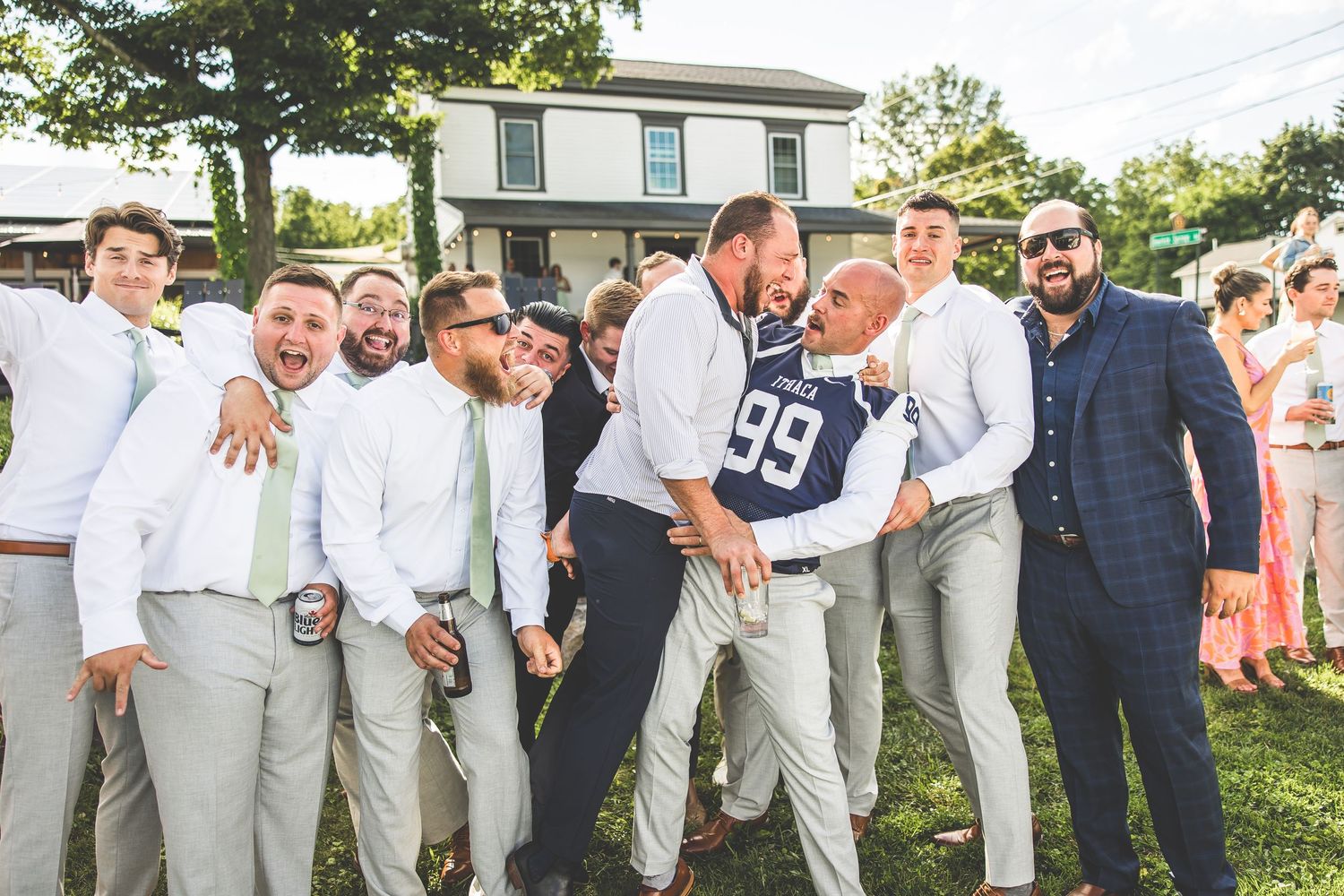 Groomsmen in light gray suits posing together at an outdoor wedding celebration.