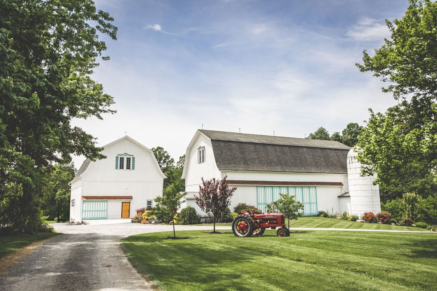 White farm buildings and a red tractor set against a blue summer sky.