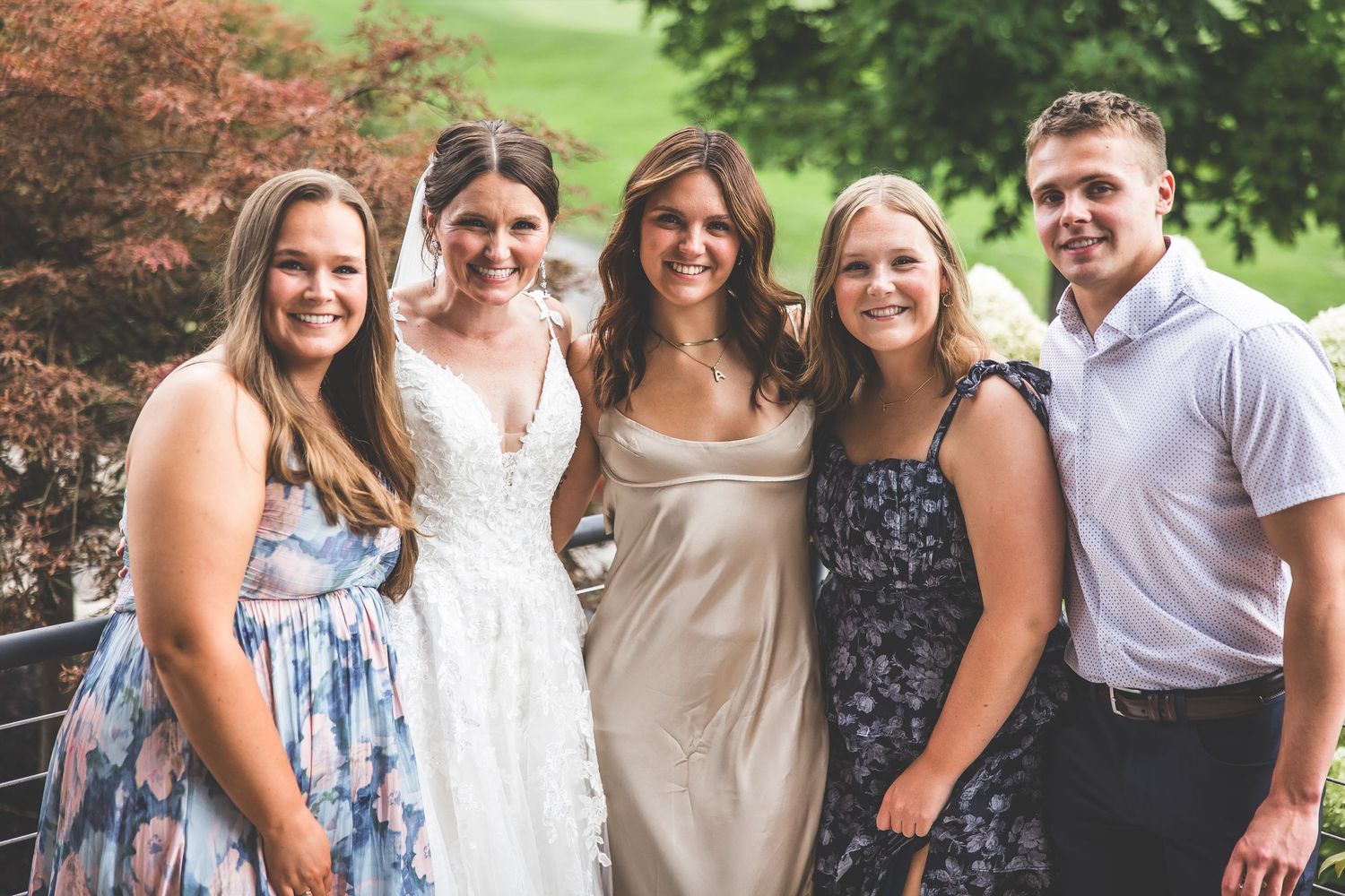 A group poses together outdoors wearing floral and pastel dresses for a summer celebration.