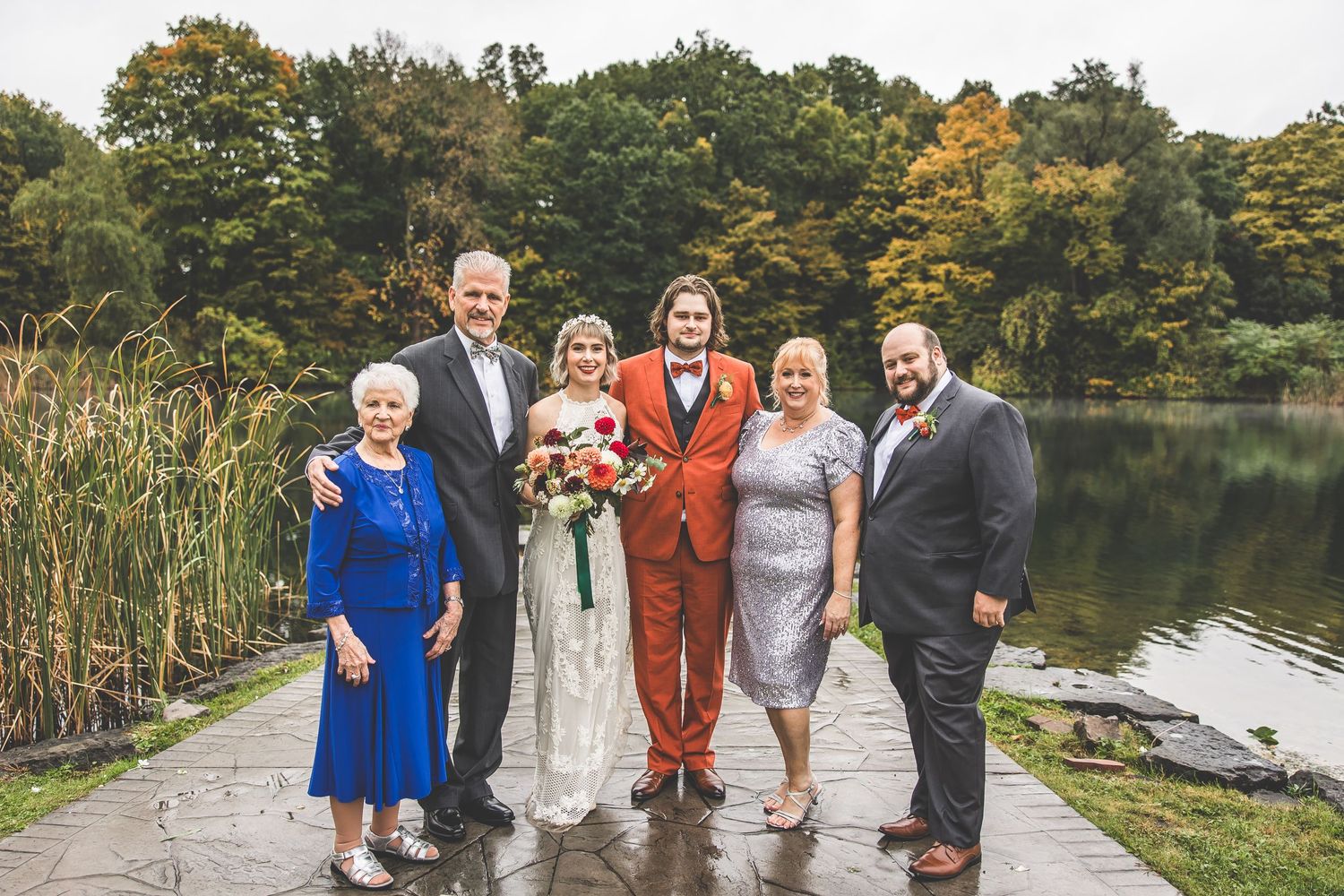 Wedding party group photo on stone dock with lake and autumn trees in background.