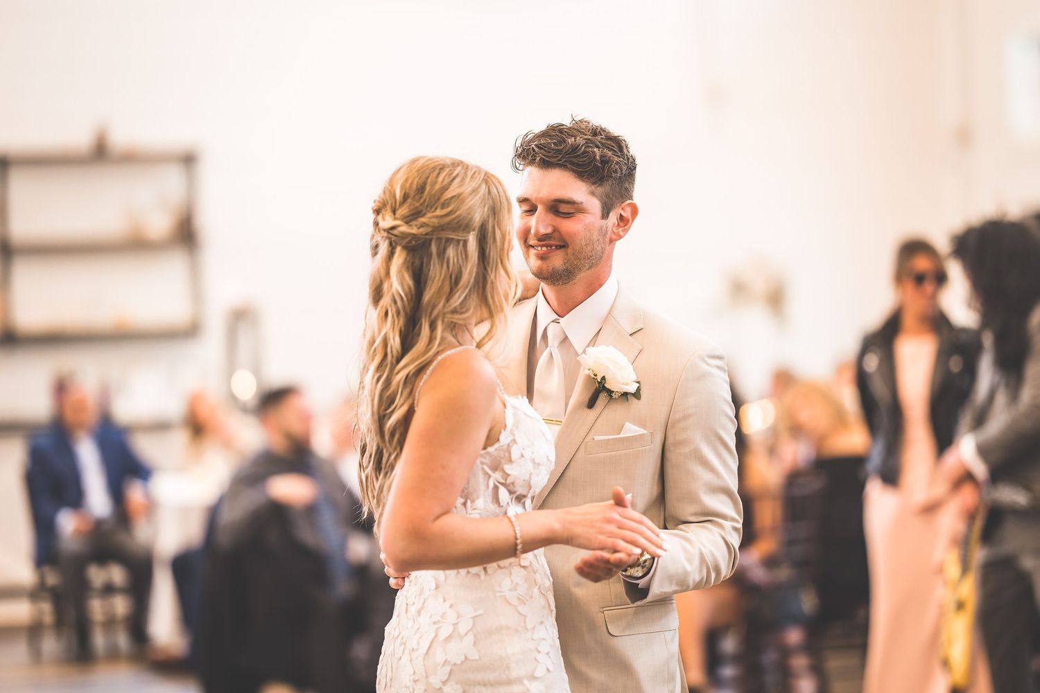 Wedding couple dances together in an intimate moment on a wooden floor surrounded by guests.