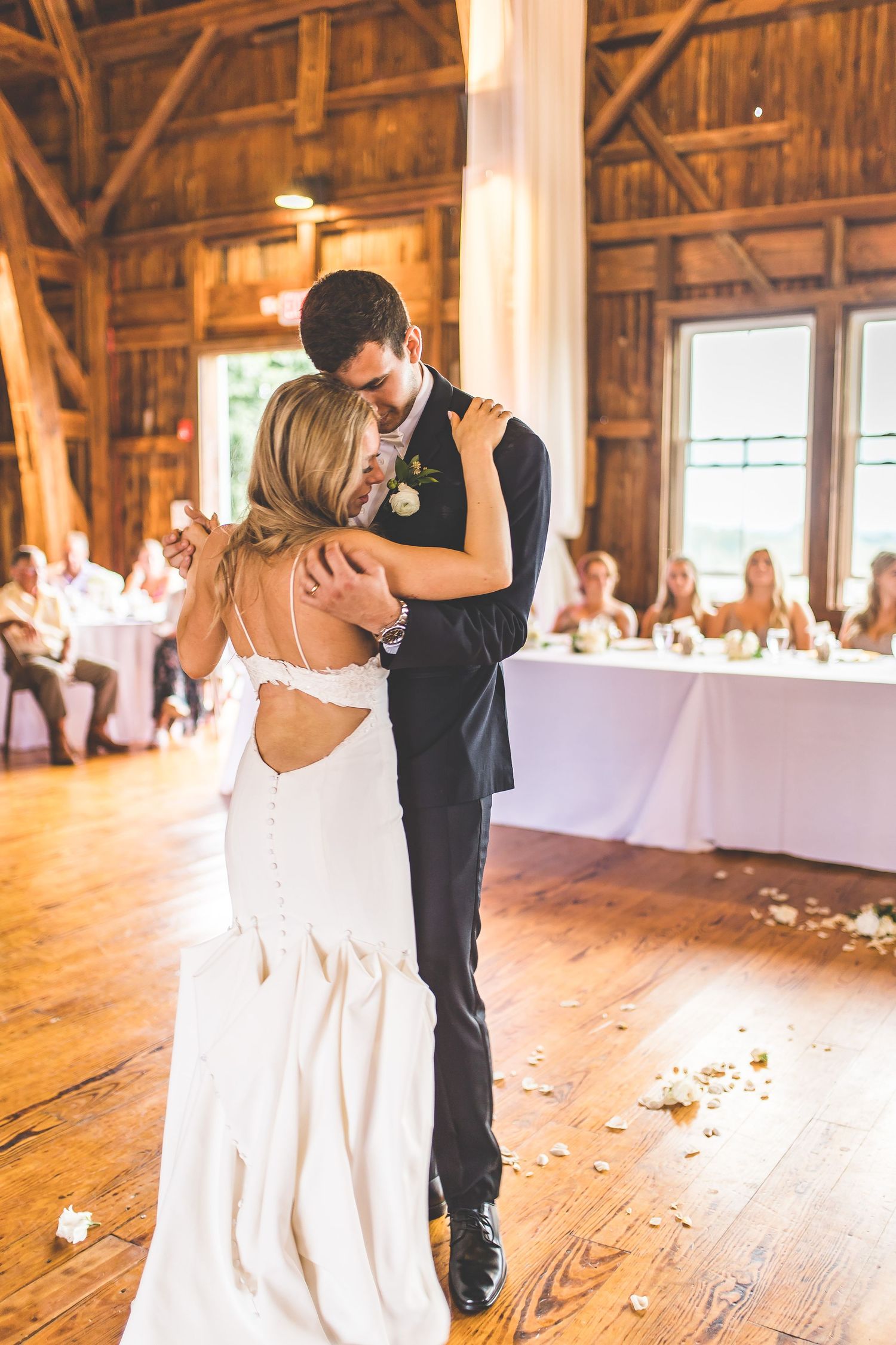 A couple shares their first dance in a rustic barn venue decorated with white draping and string lights.