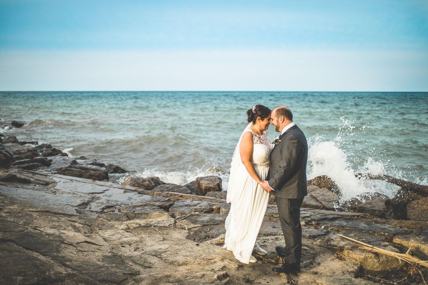 Romantic coastal wedding photos on rocky beach with waves crashing.
