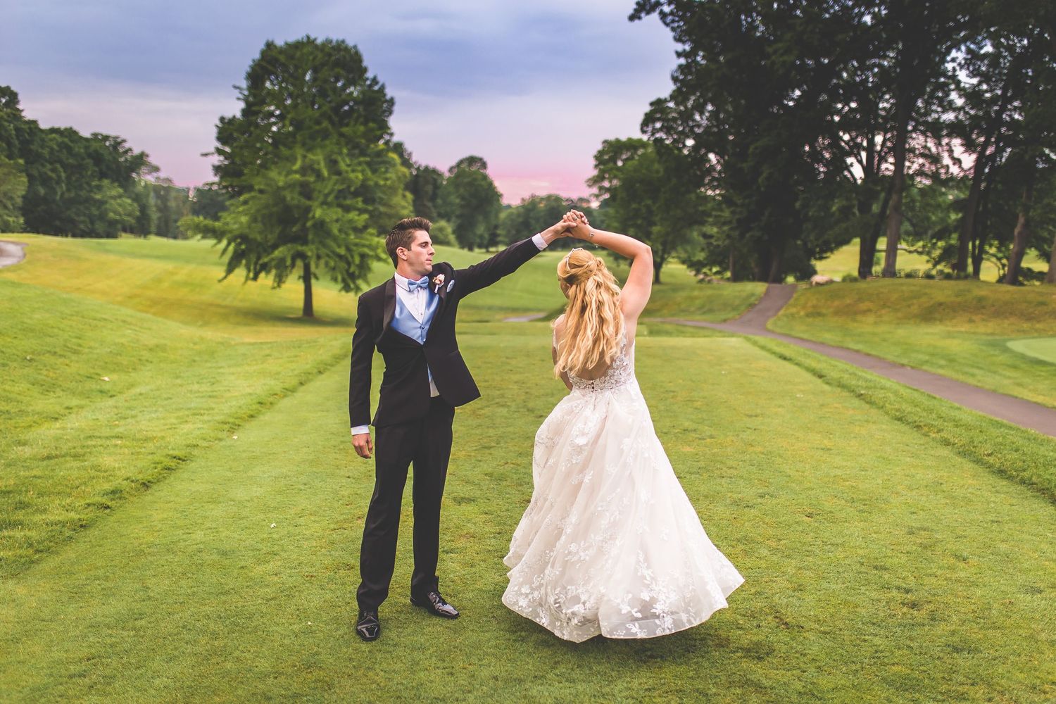 A couple shares a romantic dance on rolling hills of a golf course.