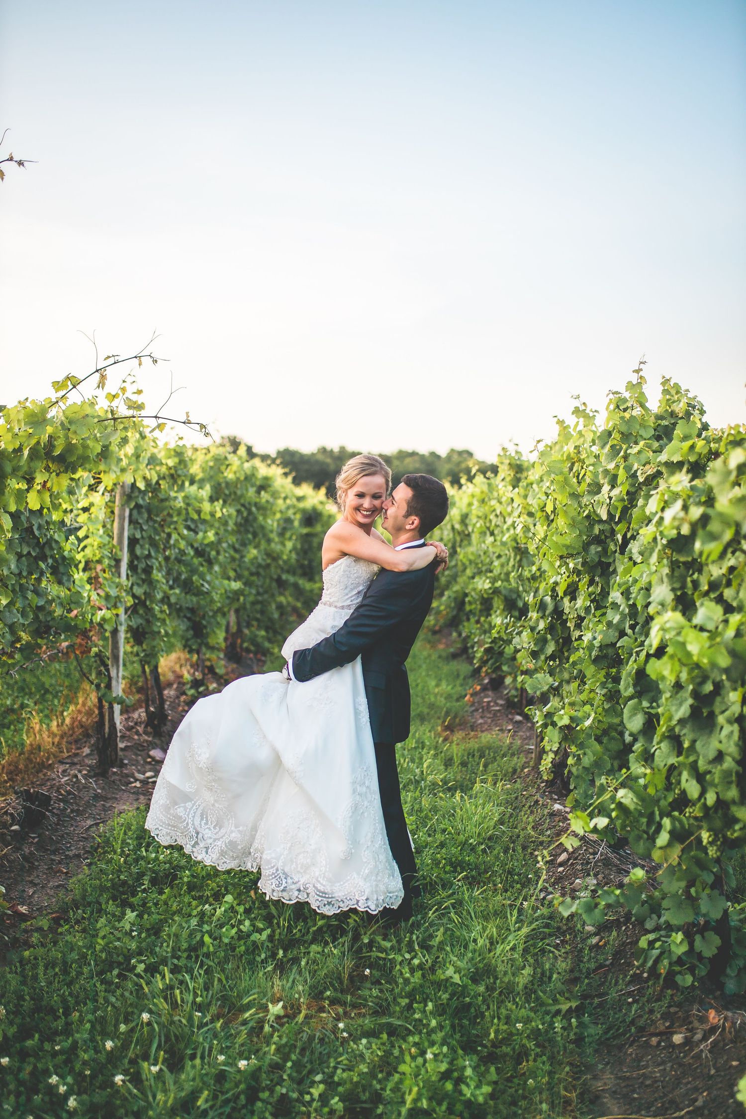A romantic couple shares a playful moment in a sunlit vineyard during their wedding photoshoot.