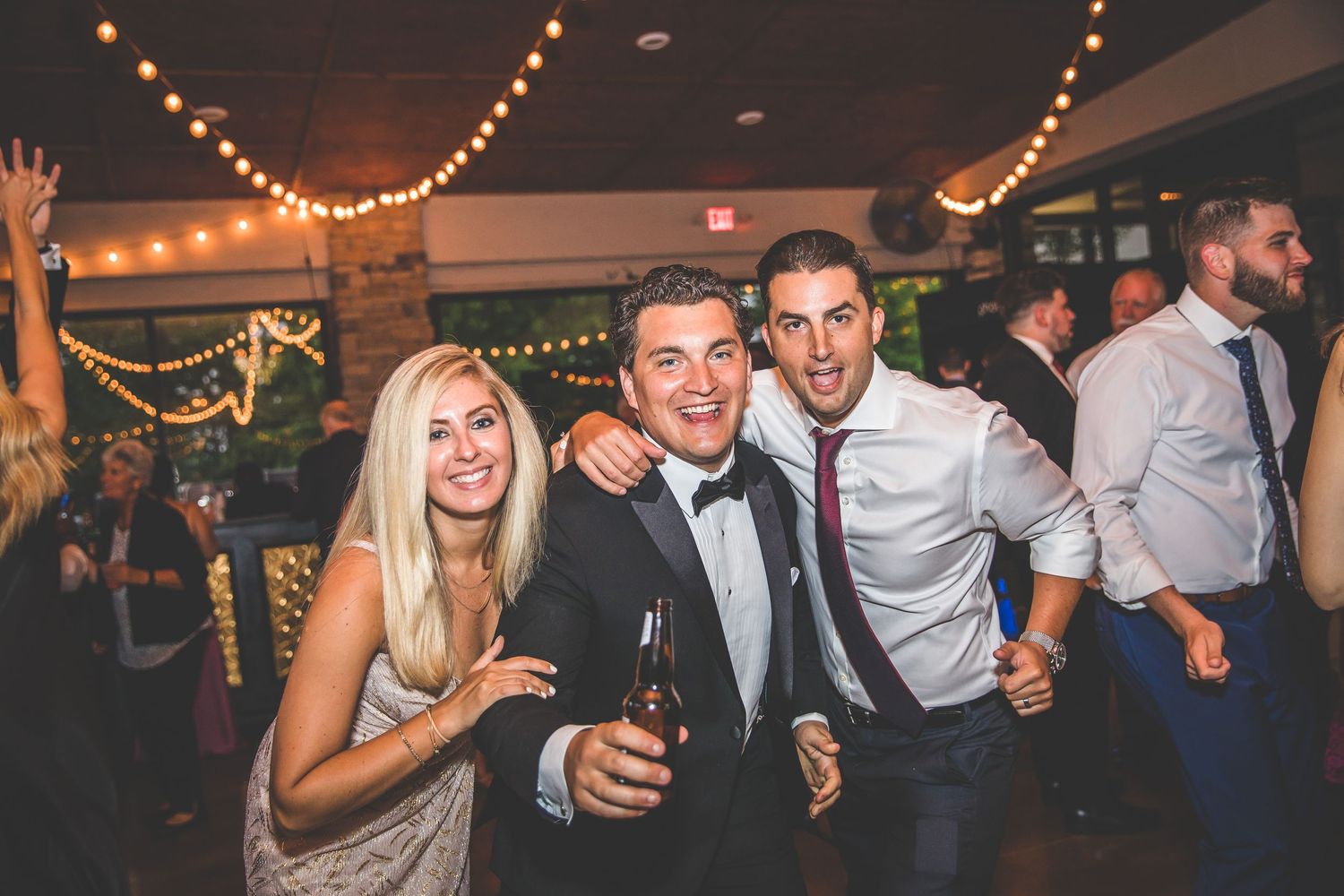 Lively wedding reception with guests dancing and celebrating under decorative lighting.