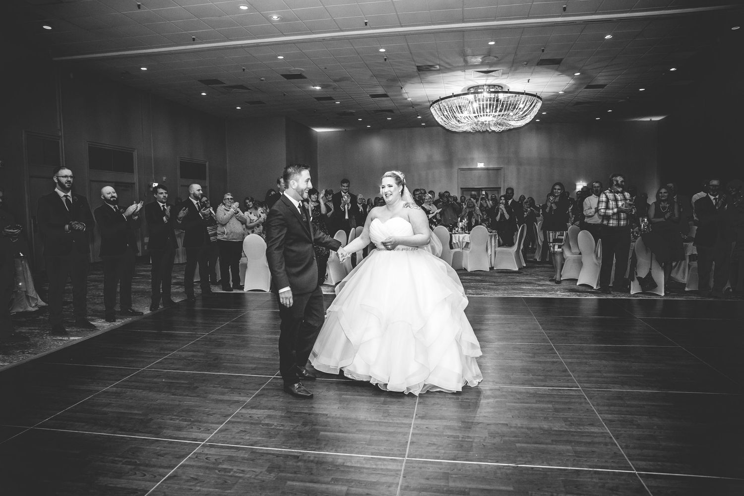 Black and white panoramic view of wedding guests dancing in a spacious ballroom.