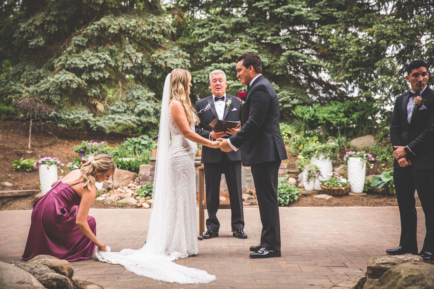 Outdoor wedding ceremony taking place on a stone patio surrounded by greenery.
