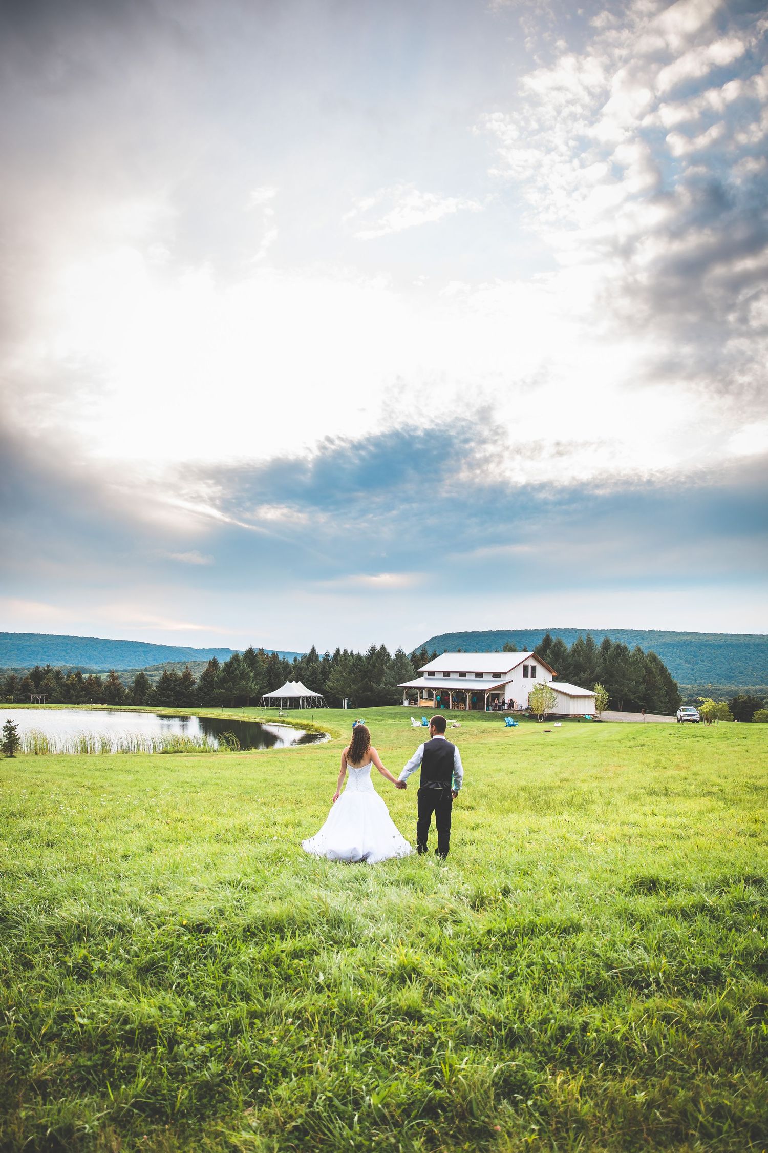 Wedding couple walking through a scenic green meadow with rolling hills and farmland in the distance.