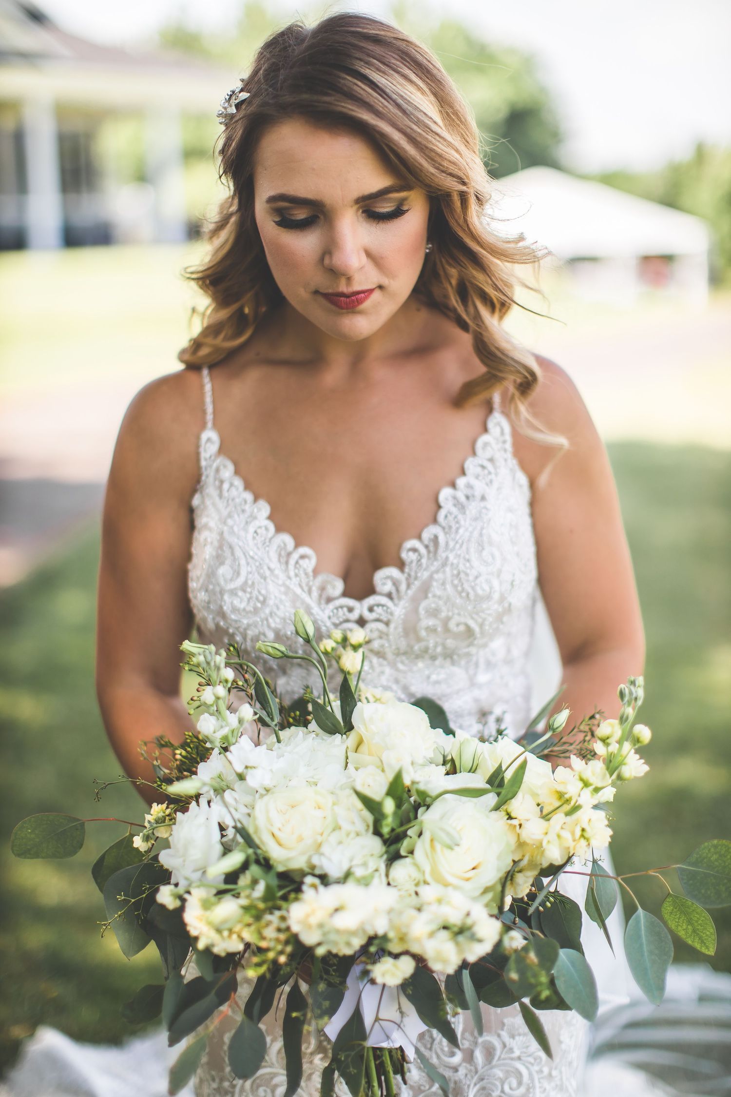 Beautiful white and cream bridal bouquet with roses and greenery against a soft outdoor background.