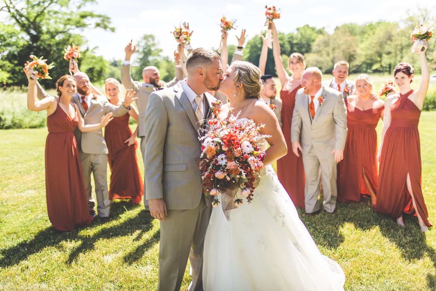 Wedding party in rust colored dresses celebrates on sunny lawn.