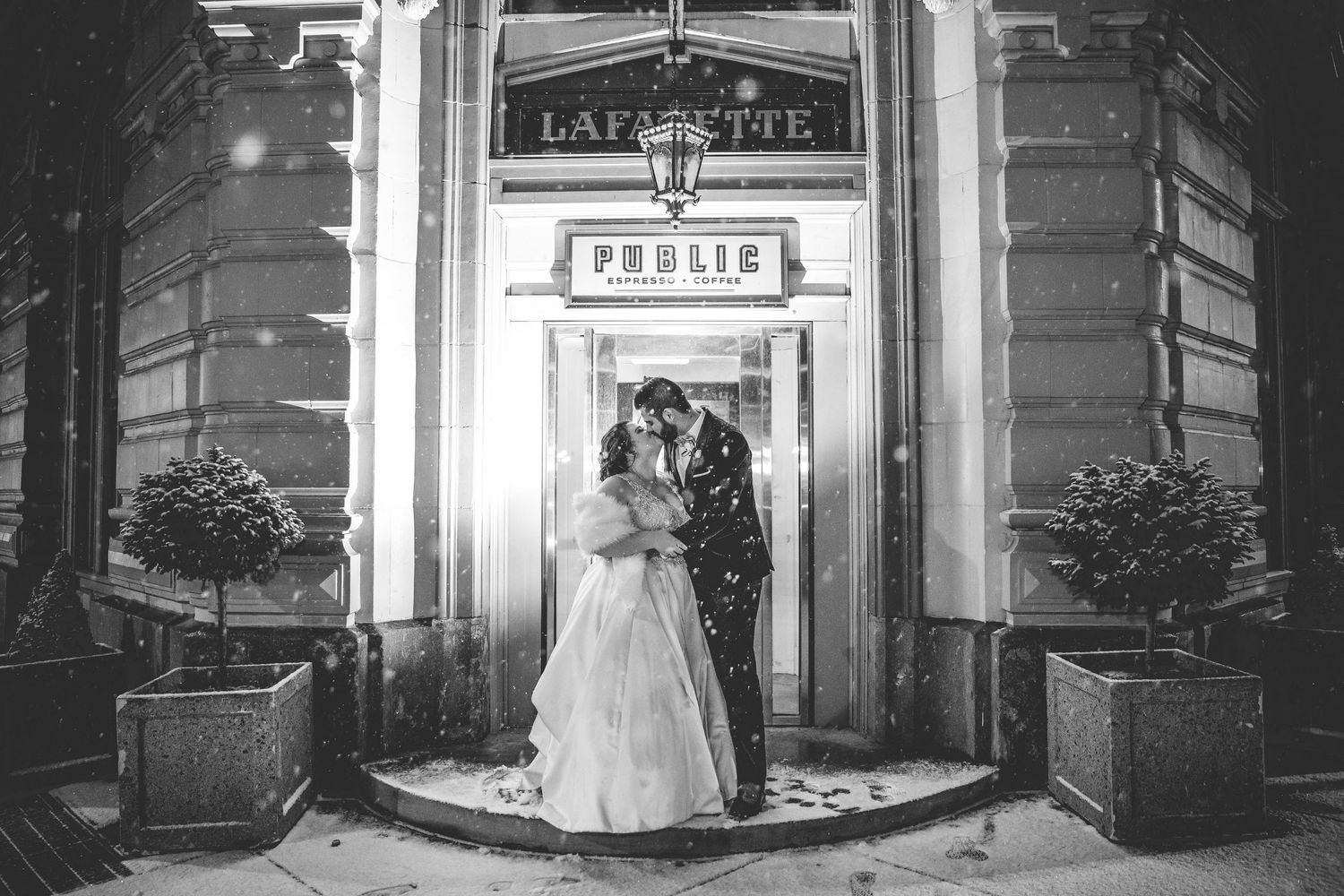 Black and white photo of a snowy winter wedding scene with decorative outdoor lighting.