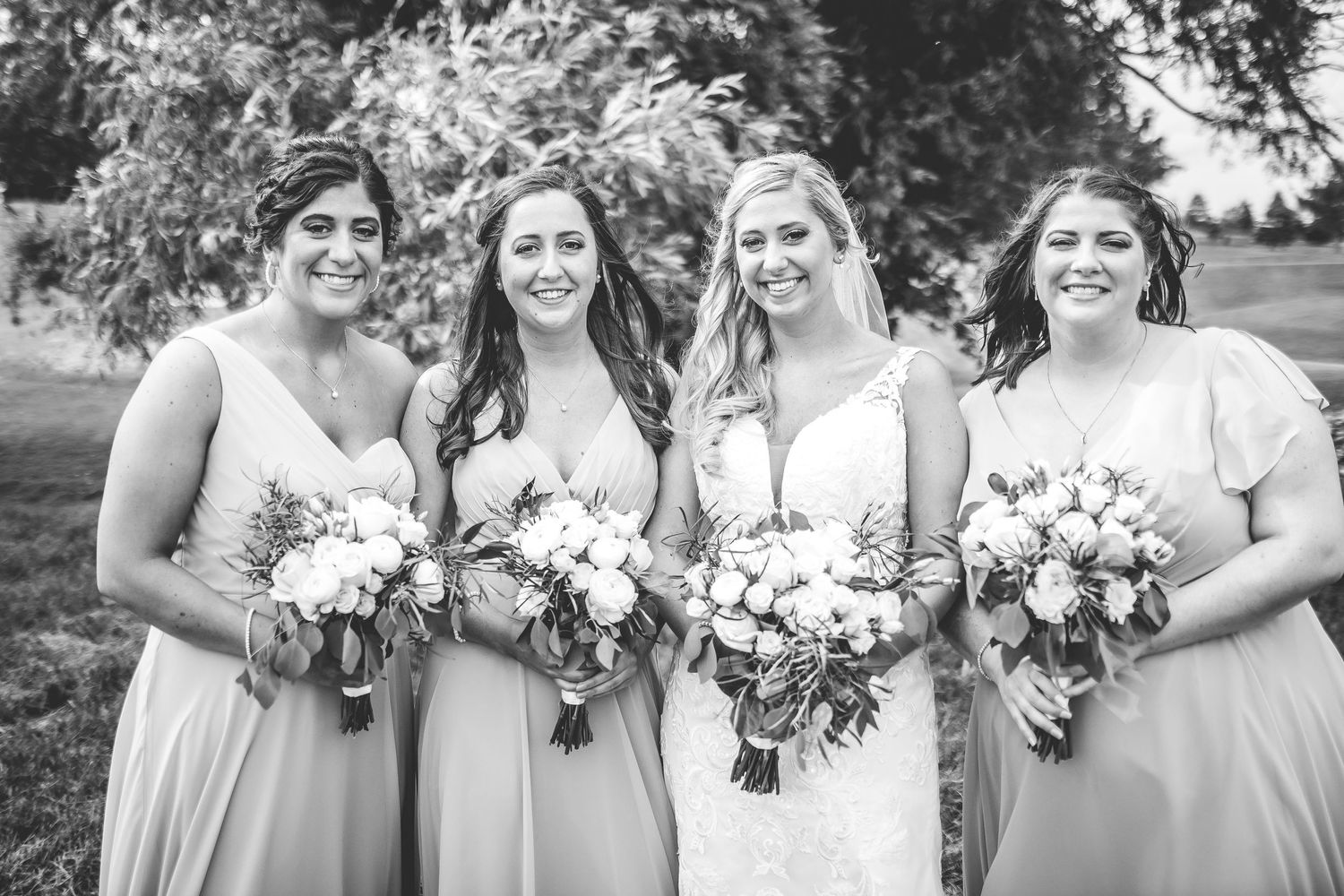 Black and white portrait of bridal party holding bouquets outdoors.