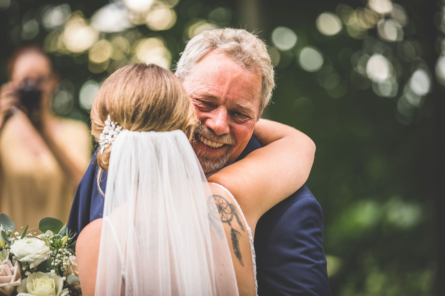 Emotional embrace between a bride in a white veil and a guest at an outdoor wedding ceremony.