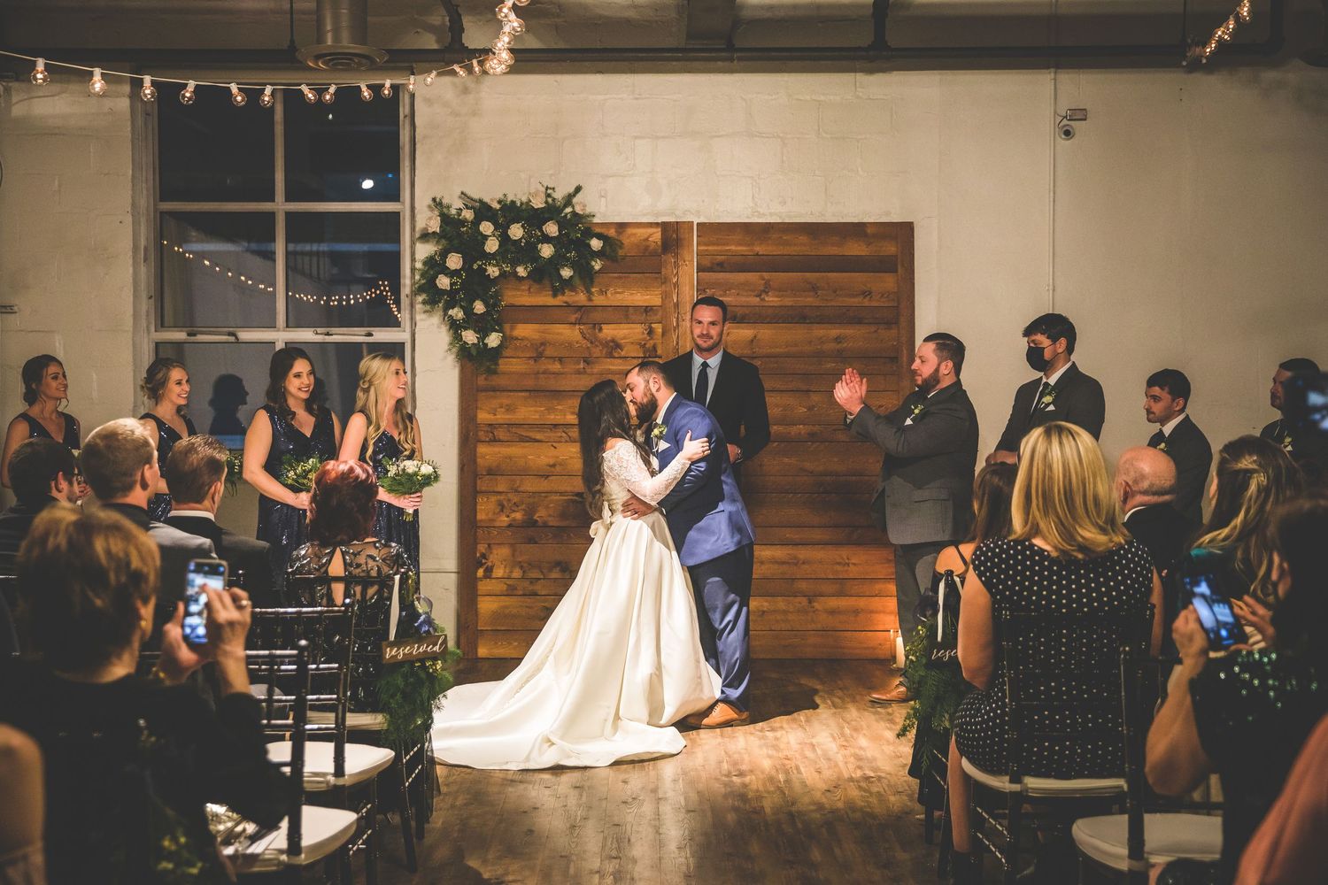 Wedding reception in an industrial space with string lights and wooden accent walls.