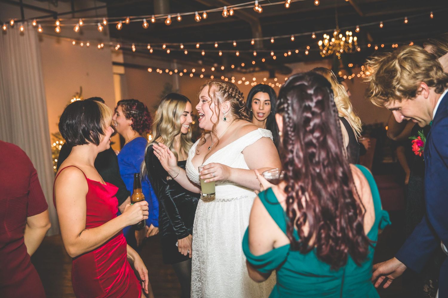 Wedding reception dance floor filled with guests under twinkling string lights.