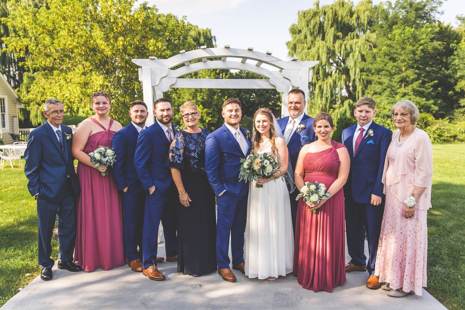 Full wedding party lineup with children in formal attire posed under an outdoor white pergola.