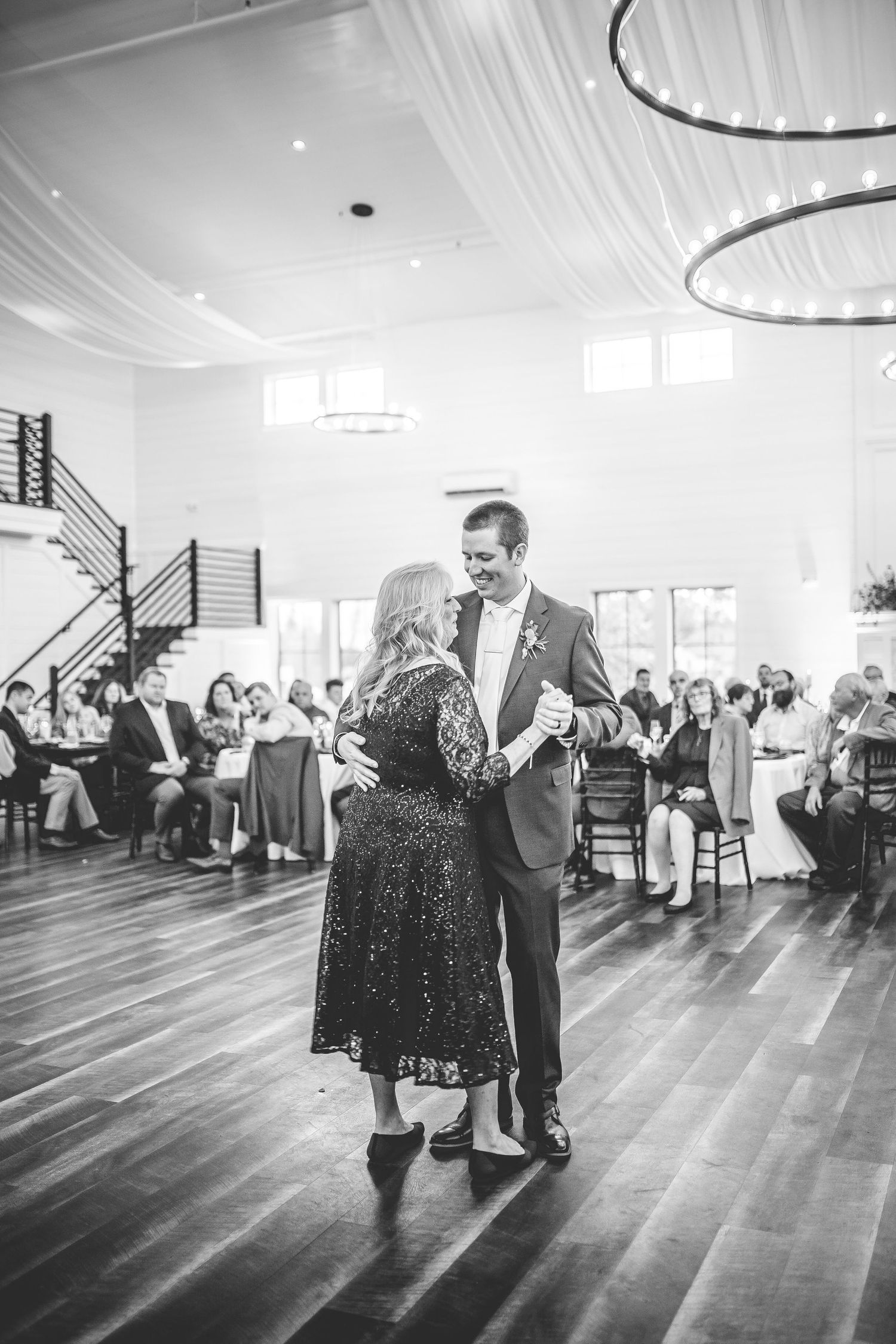 A black and white photo of a couple dancing in an elegant reception hall with draped ceiling decor.