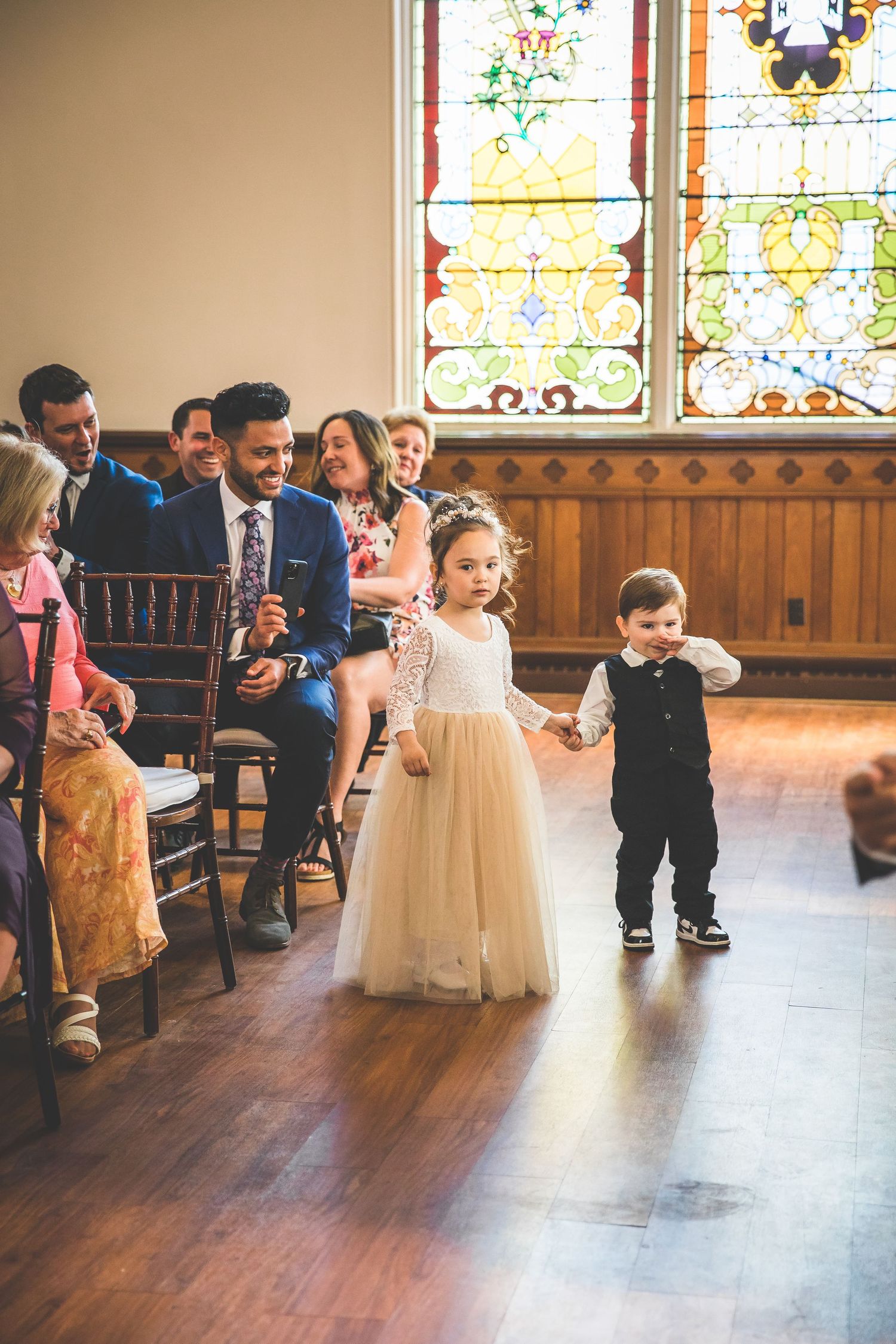 Children in formal attire playing in church hall with stained glass windows.