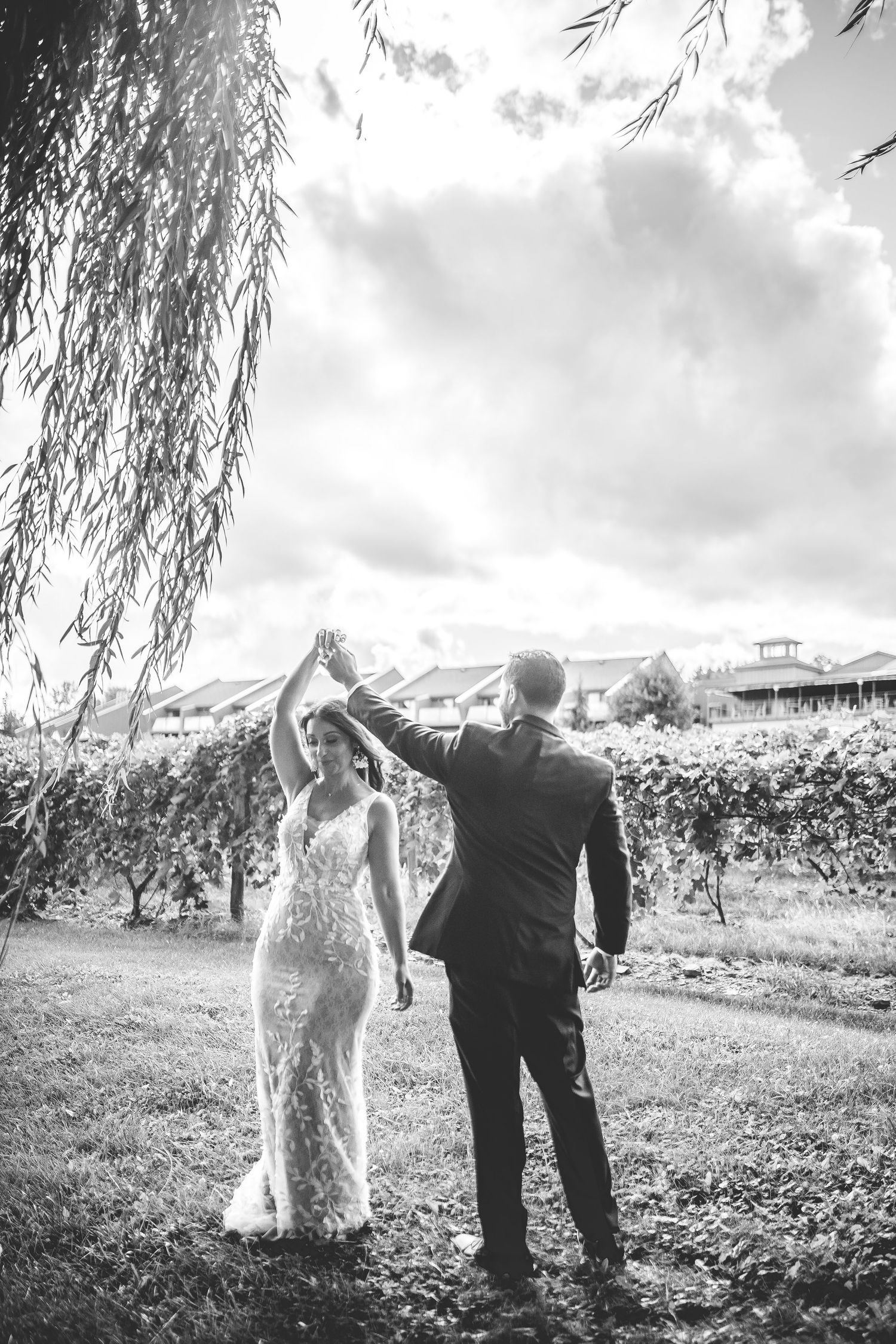 Black and white portrait of couple dancing under willow trees.