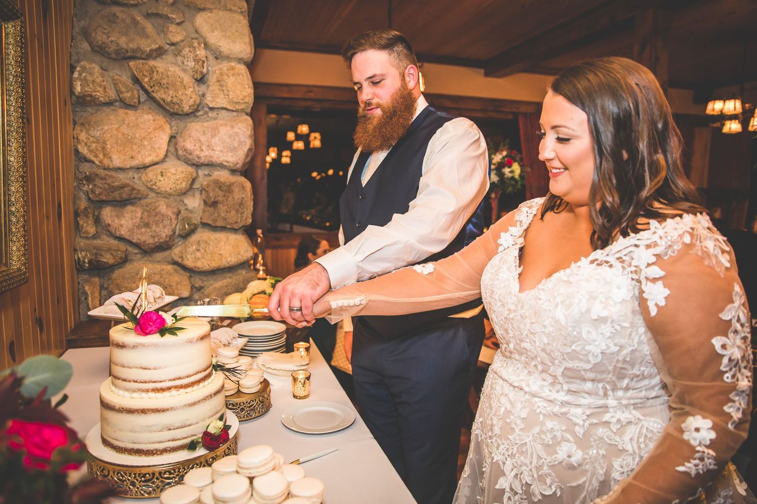 Wedding couple cuts their rustic wedding cake together in an intimate indoor venue with stone walls.