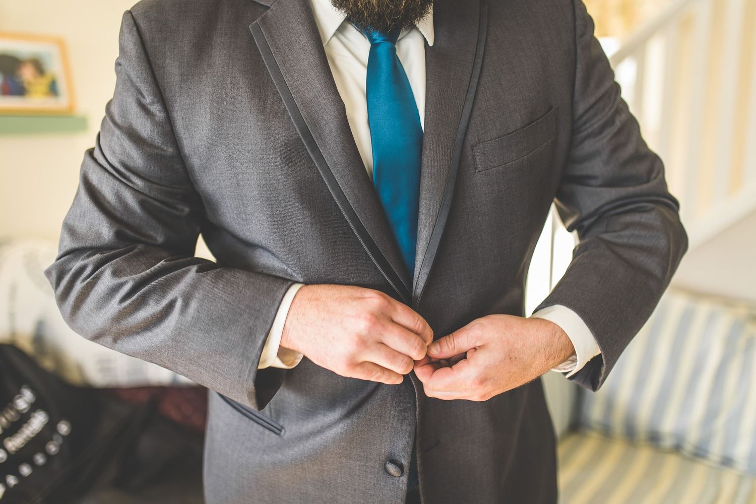 Man in gray suit and blue tie adjusts his cuffs.