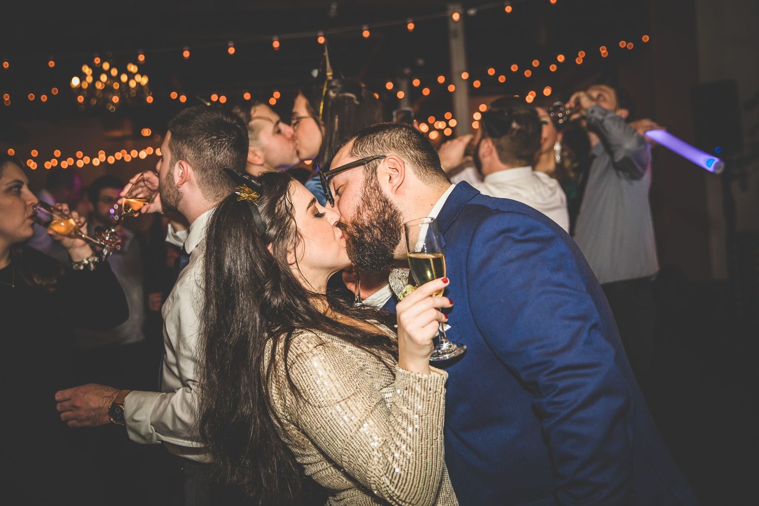 Couple shares an intimate first look moment at a rustic venue with twinkling lights in the background.