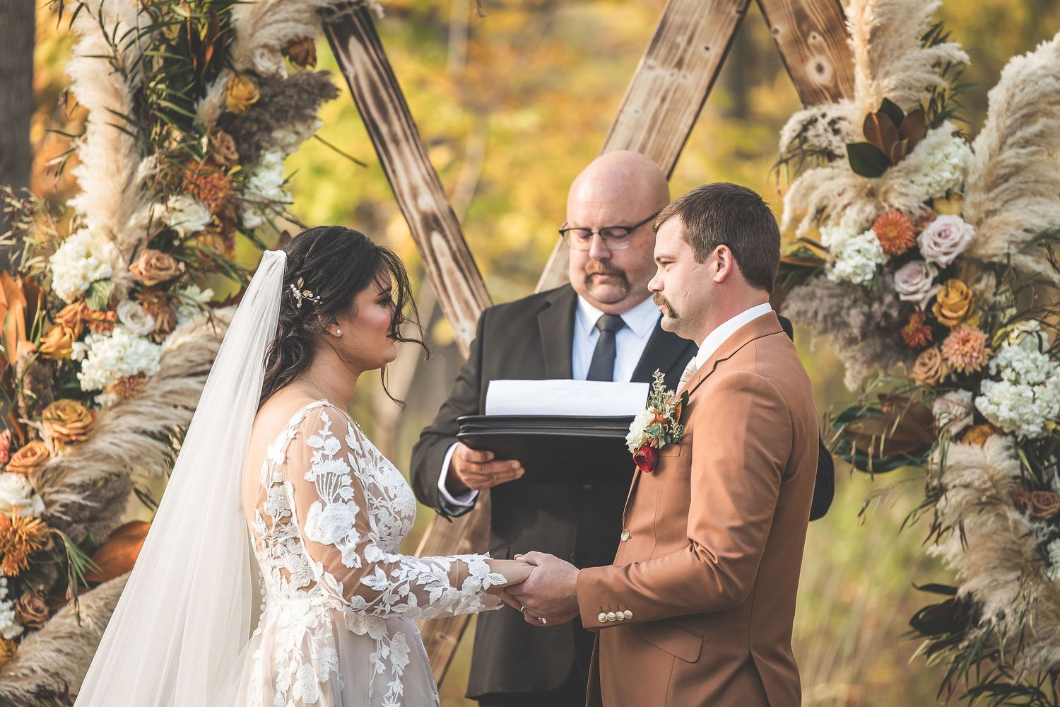 Intimate wedding ceremony moment captured in wooded setting with autumn colors.