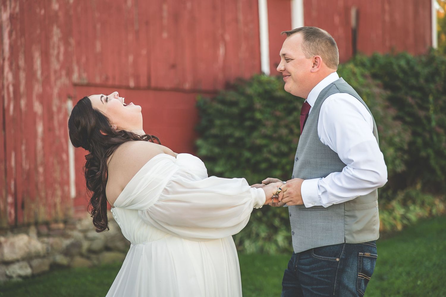 Wedding couple shares intimate moments in front of weathered red barn wall.