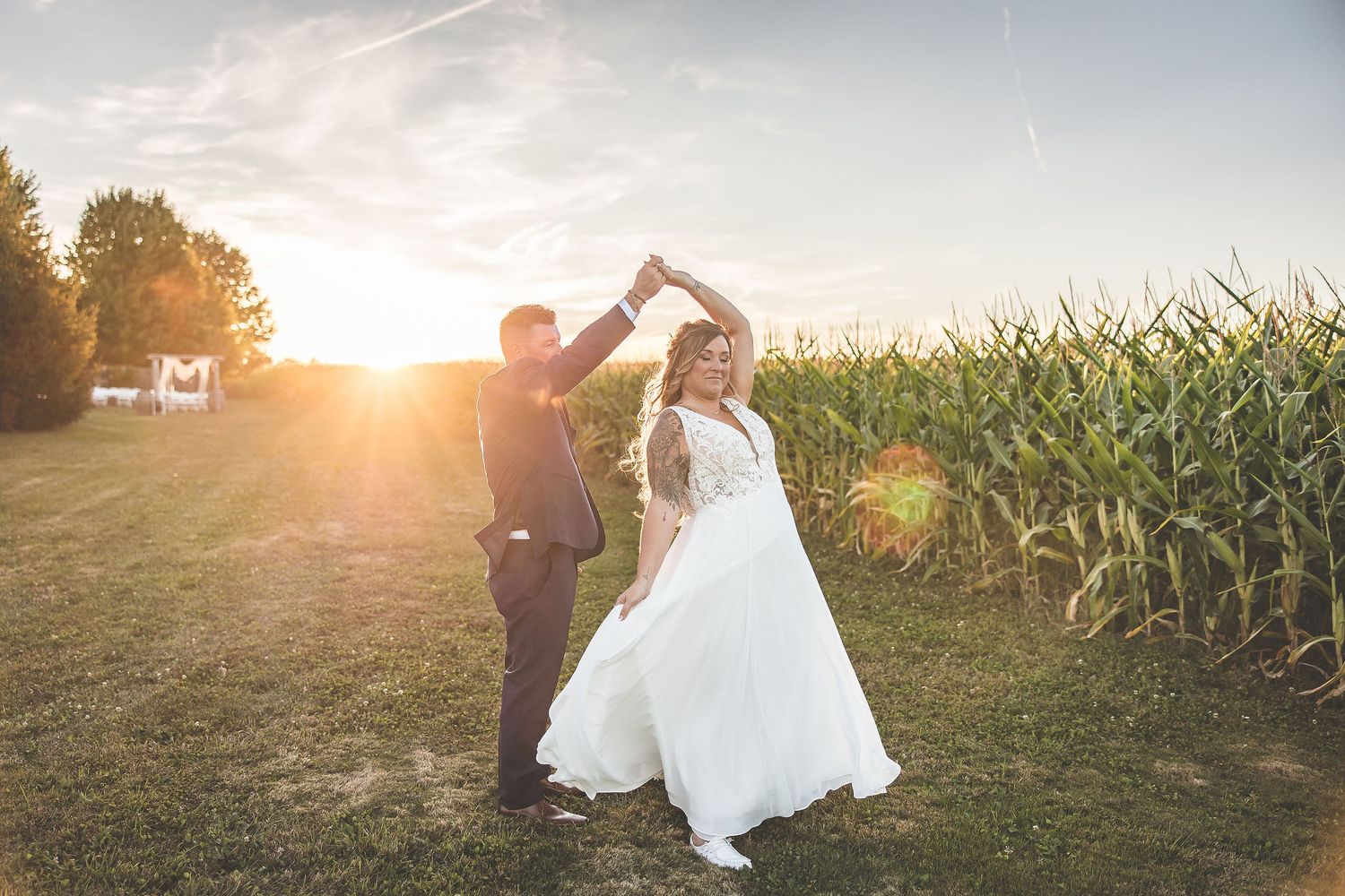 Wedding couple poses in front of cornfield during golden hour sunset.