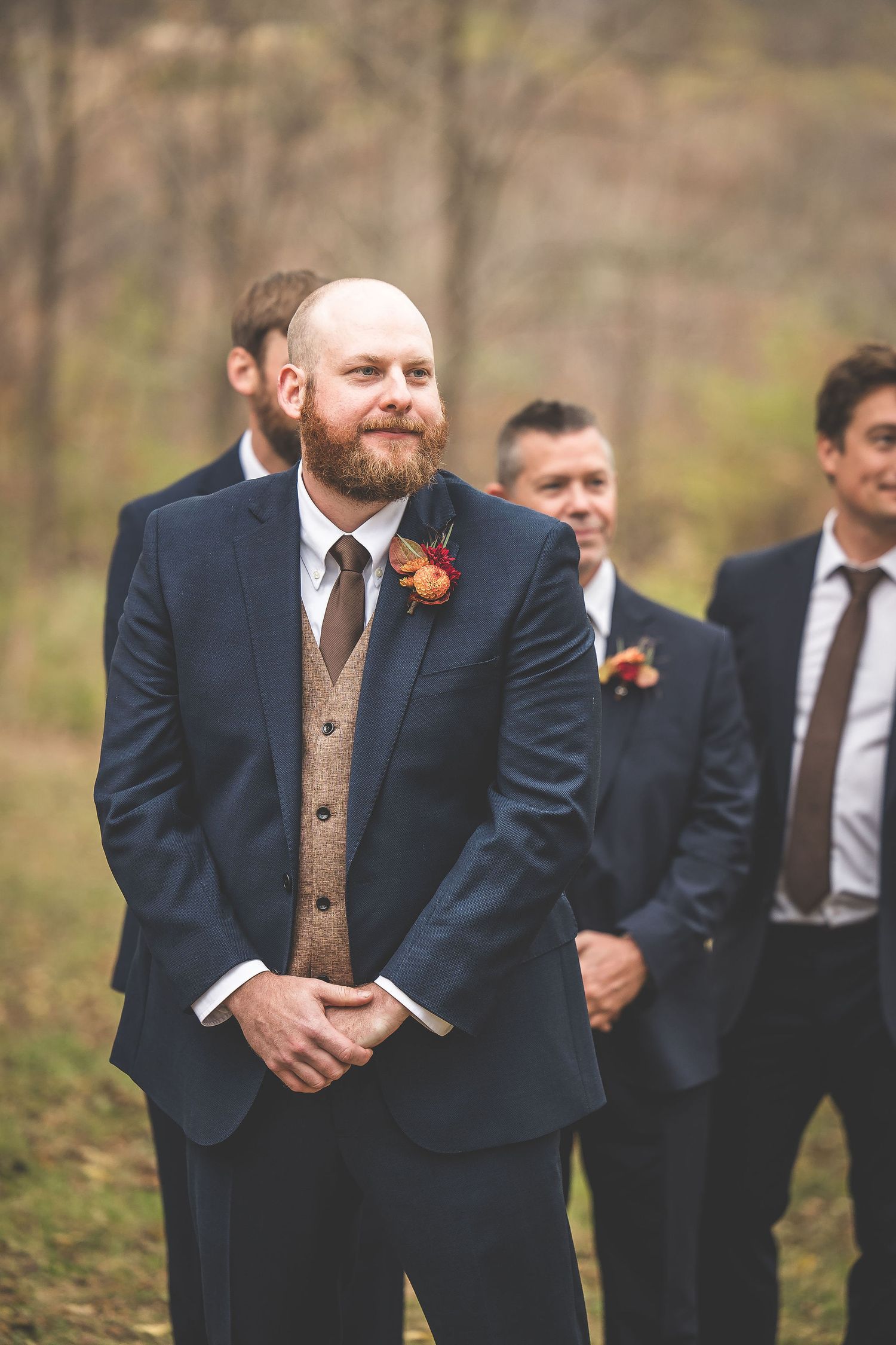 Groomsmen in navy suits and brown vests share candid moment outdoors.
